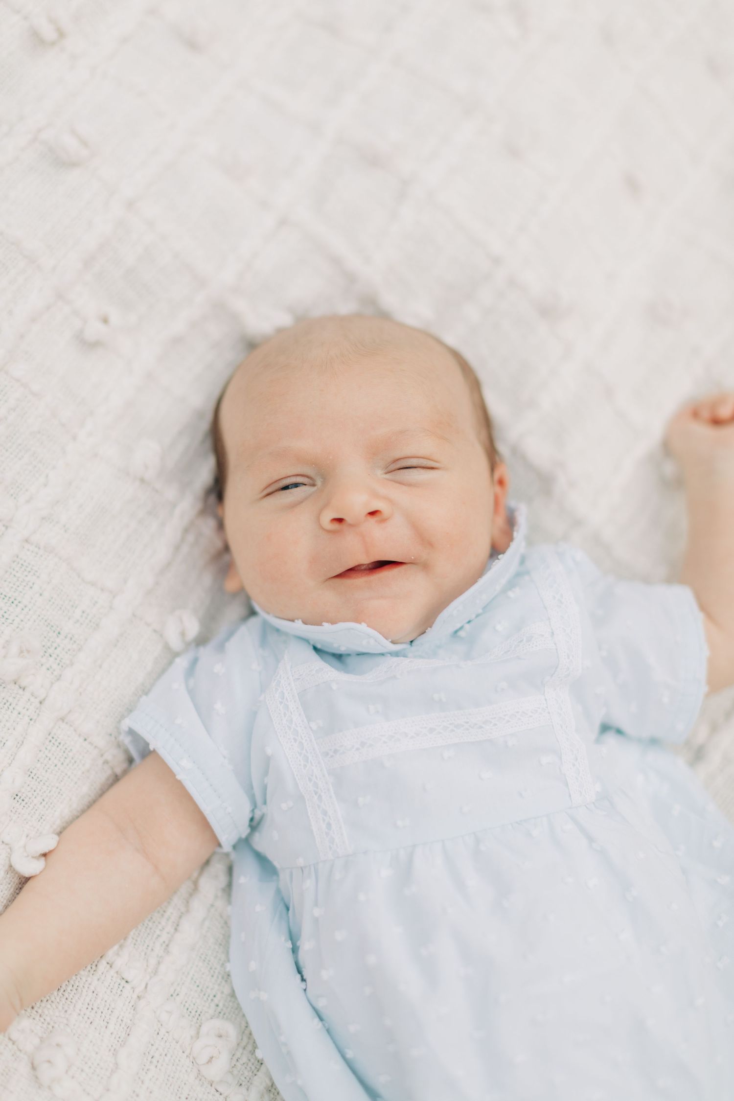 Happy baby in pale blue outfit lying on textured white fabric.