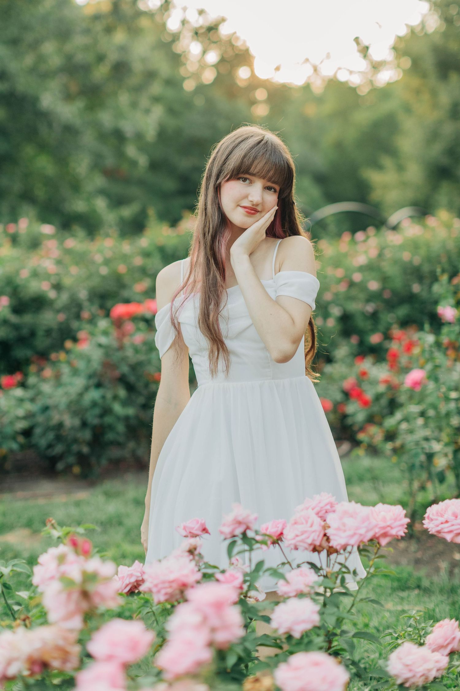 Ethereal garden scene with pink roses framing a flowing white sundress in natural sunlight.