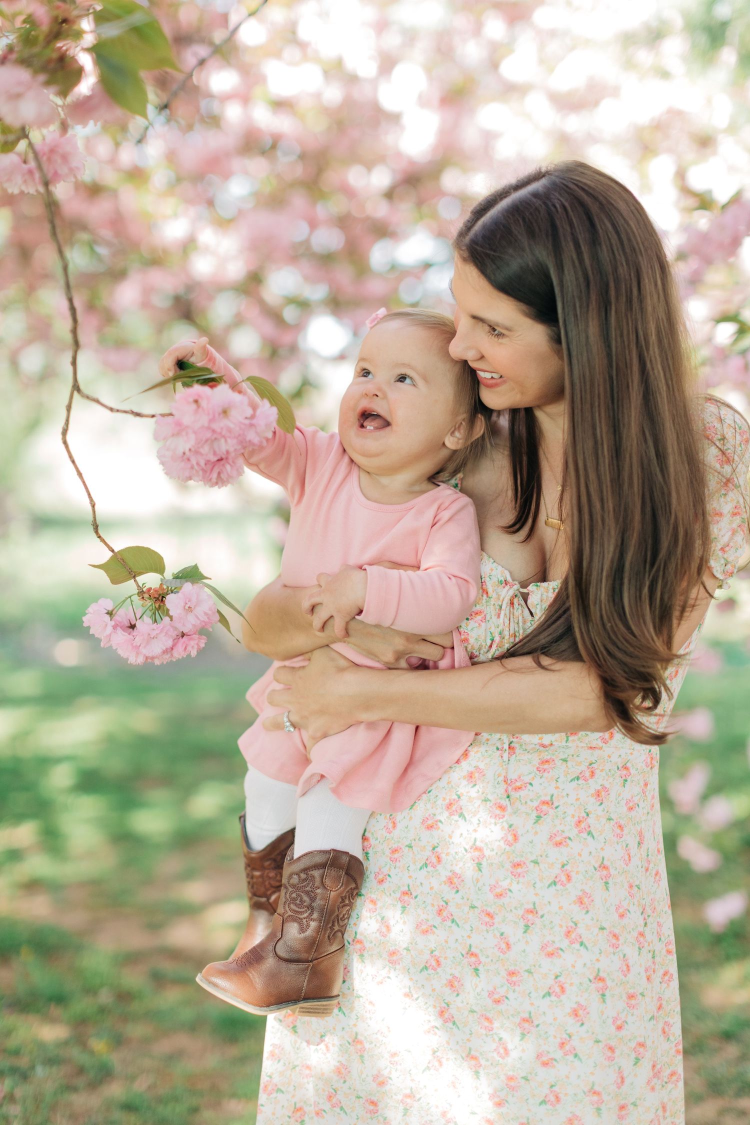 A tender moment reaching for cherry blossoms in a dreamy spring garden setting.