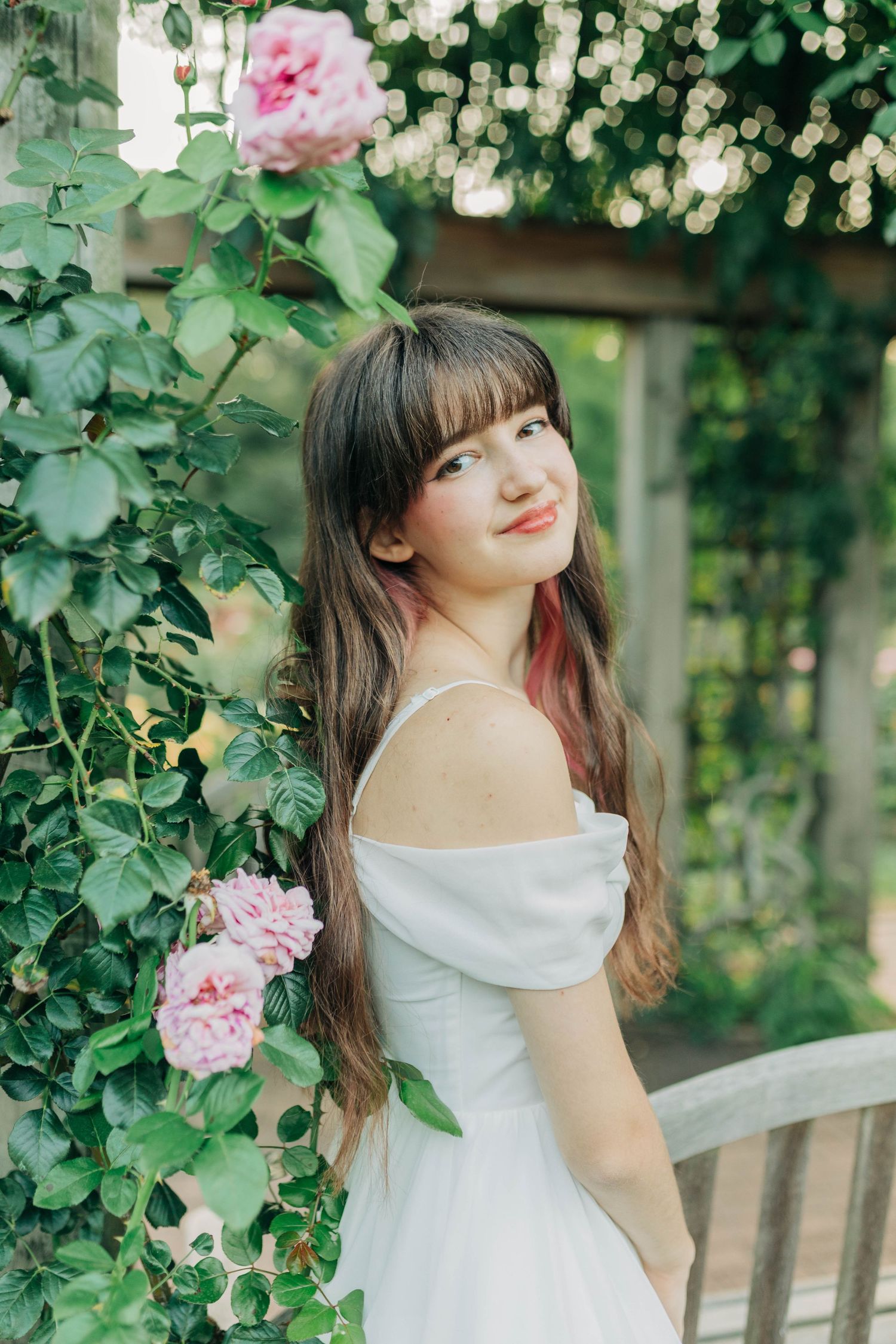 Romantic garden scene with pink roses climbing around a wooden bench and flowing white dress.