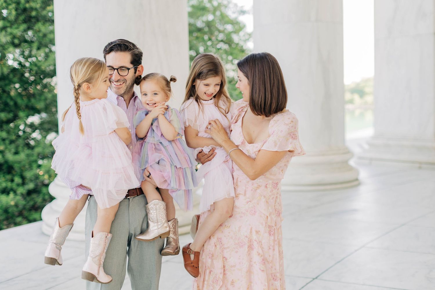 Happy family with three young girls in pink dresses posing near white columns at the Jefferson Memorial.