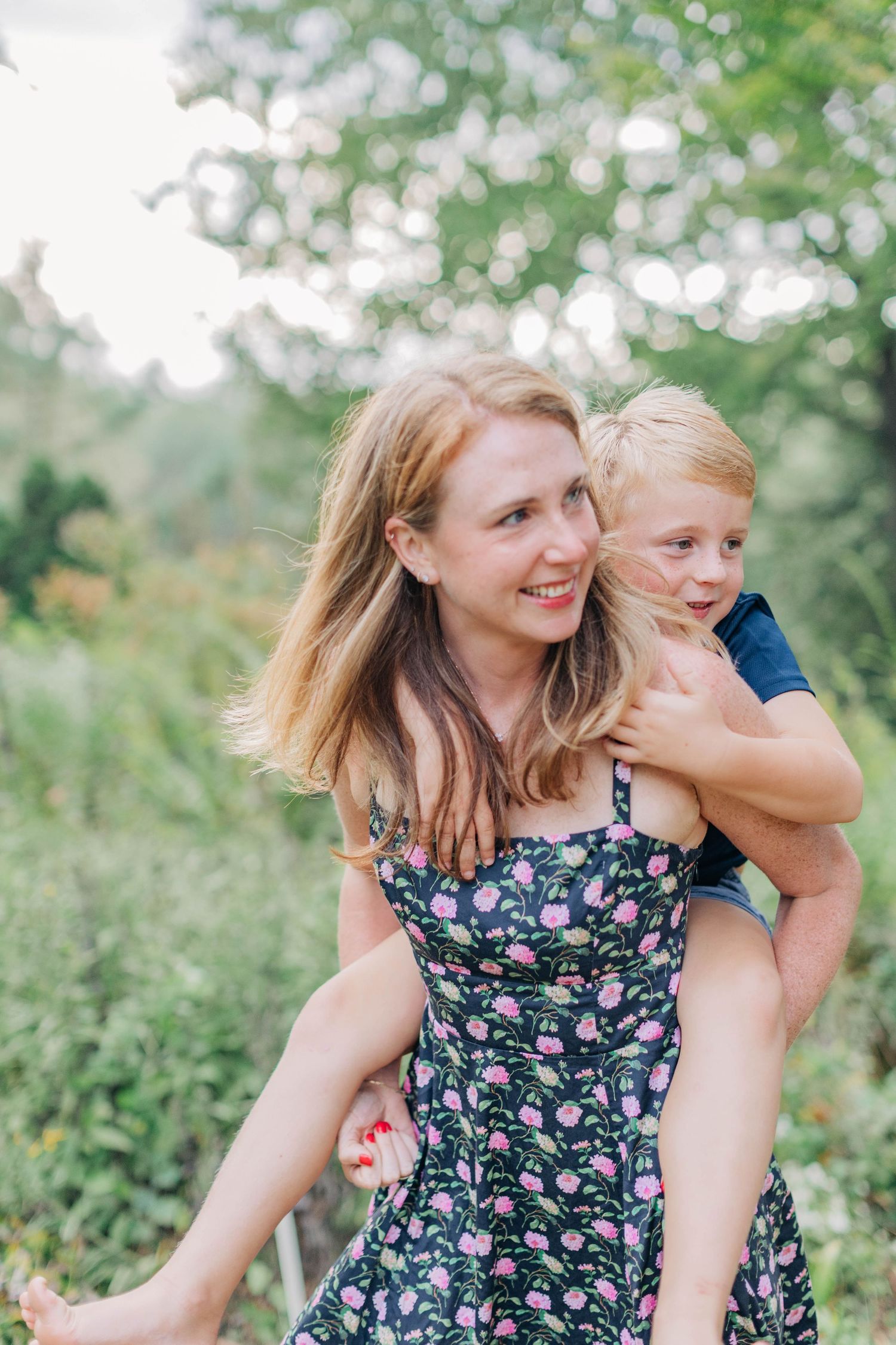 A playful piggyback ride moment captured in a sunlit garden with flowering plants in the background.