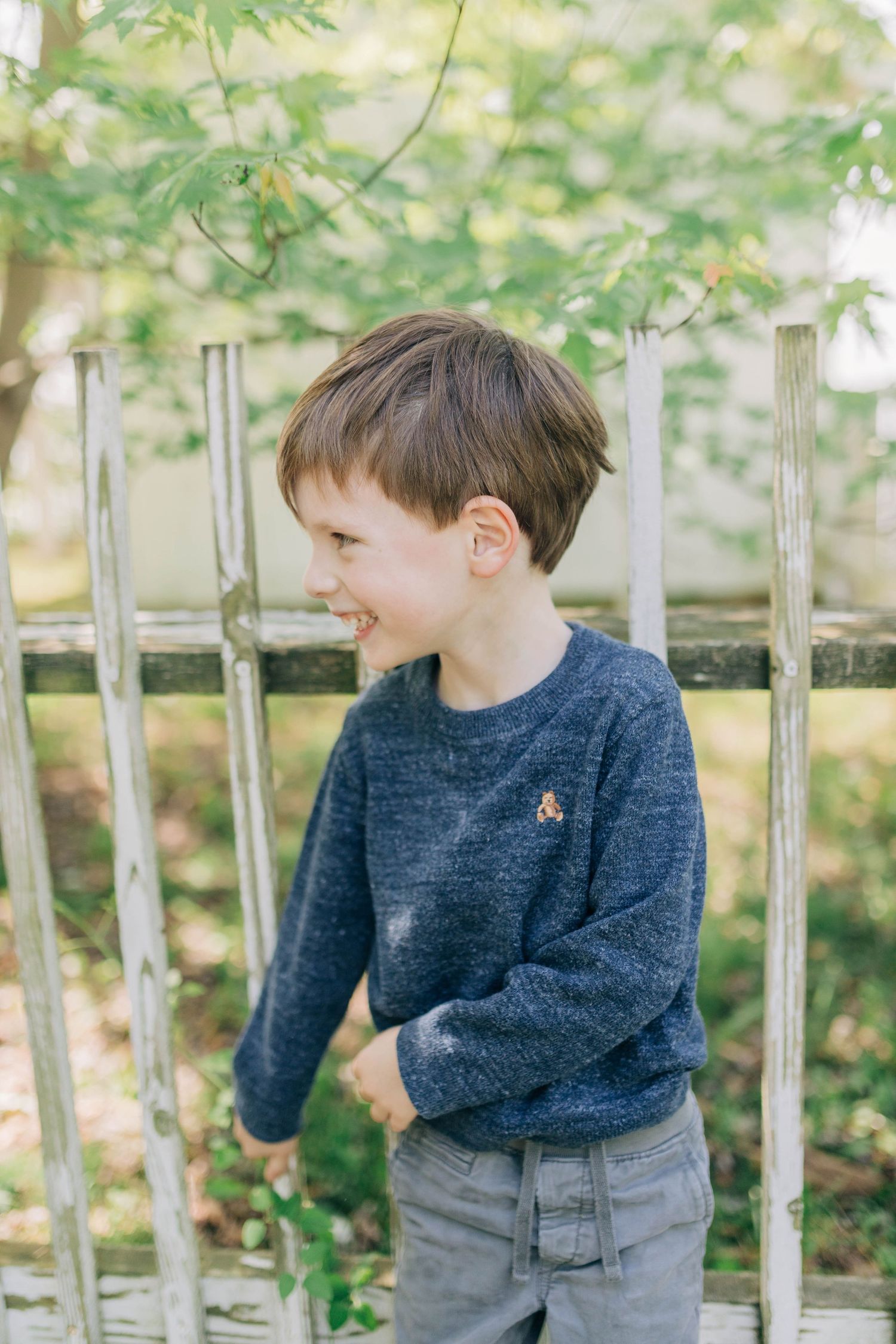 Two children in navy sweaters sharing playful moments in an outdoor garden setting.