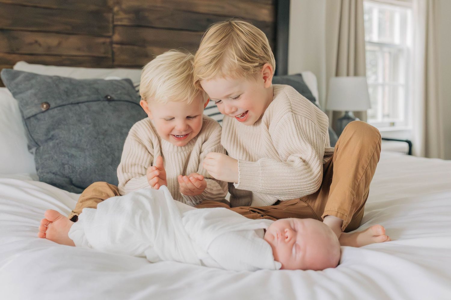 Two young children sitting on bed with newborn sibling.