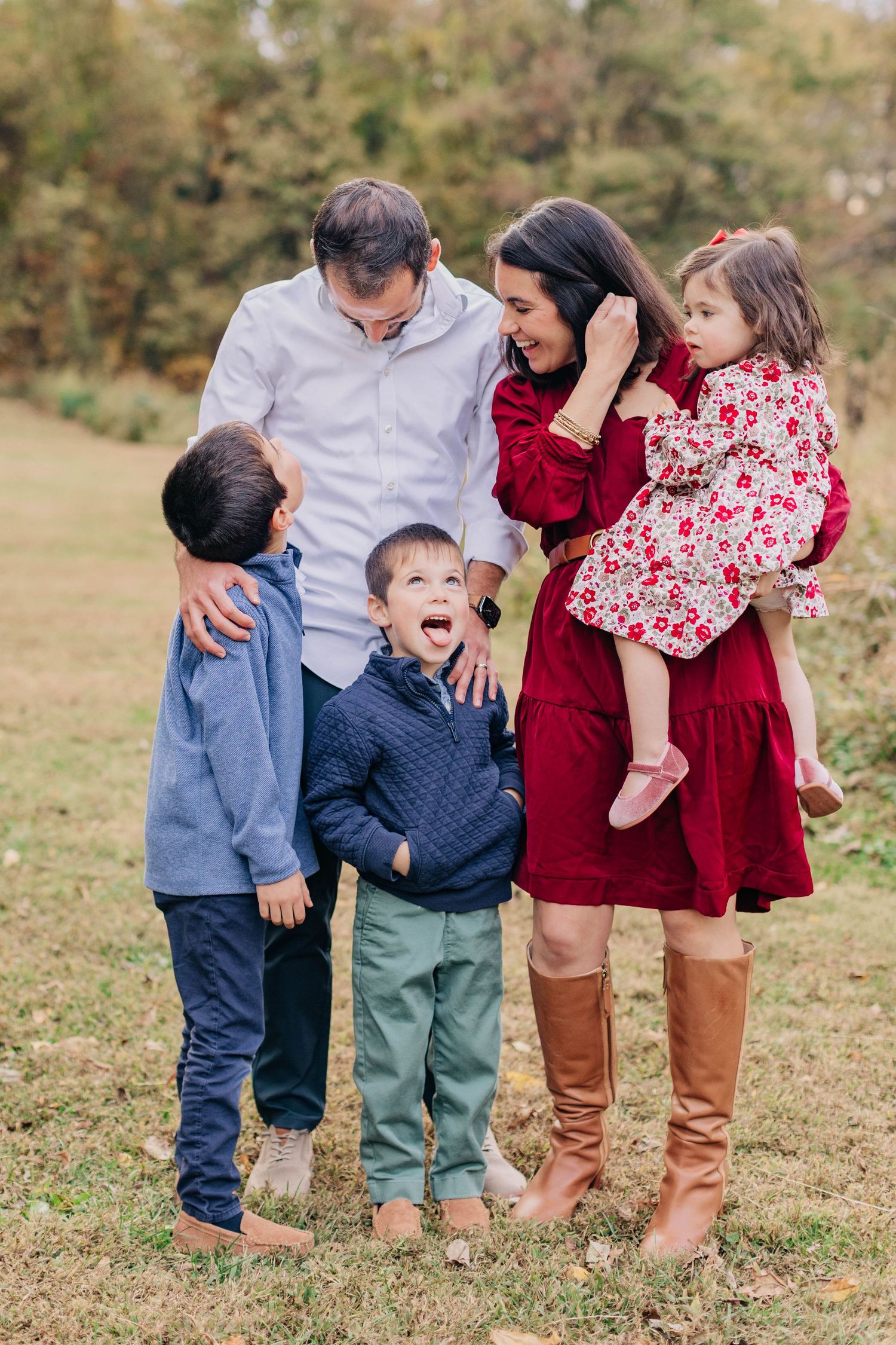A happy family of five poses outdoors in fall, wearing red and blue outfits, with parents and three young children smiling.
