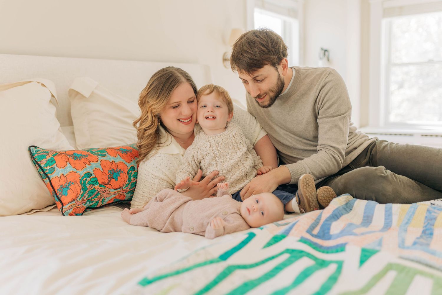 Family sharing tender moments while relaxing on a bed with striped blanket.