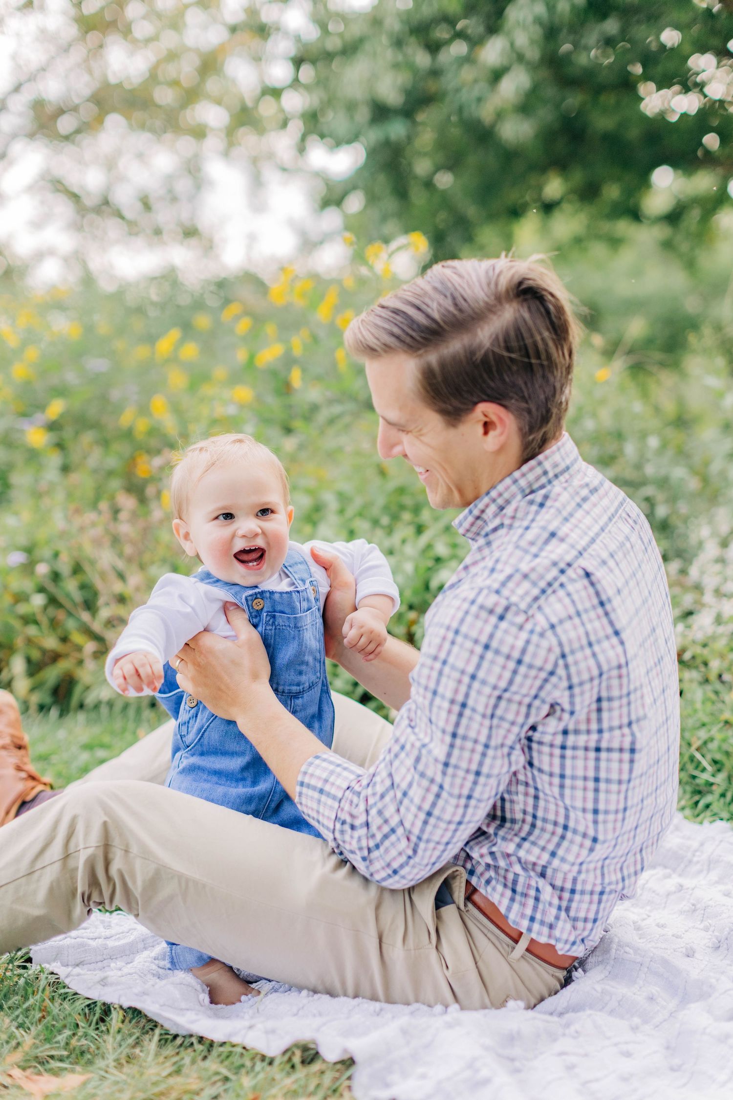 Playful interaction between parent and baby sitting on a blanket in a sunny garden.