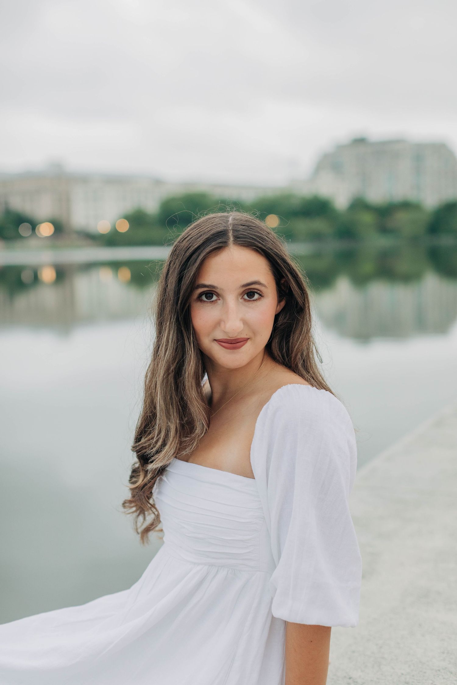 Portrait in white dress with city buildings reflecting in water behind.