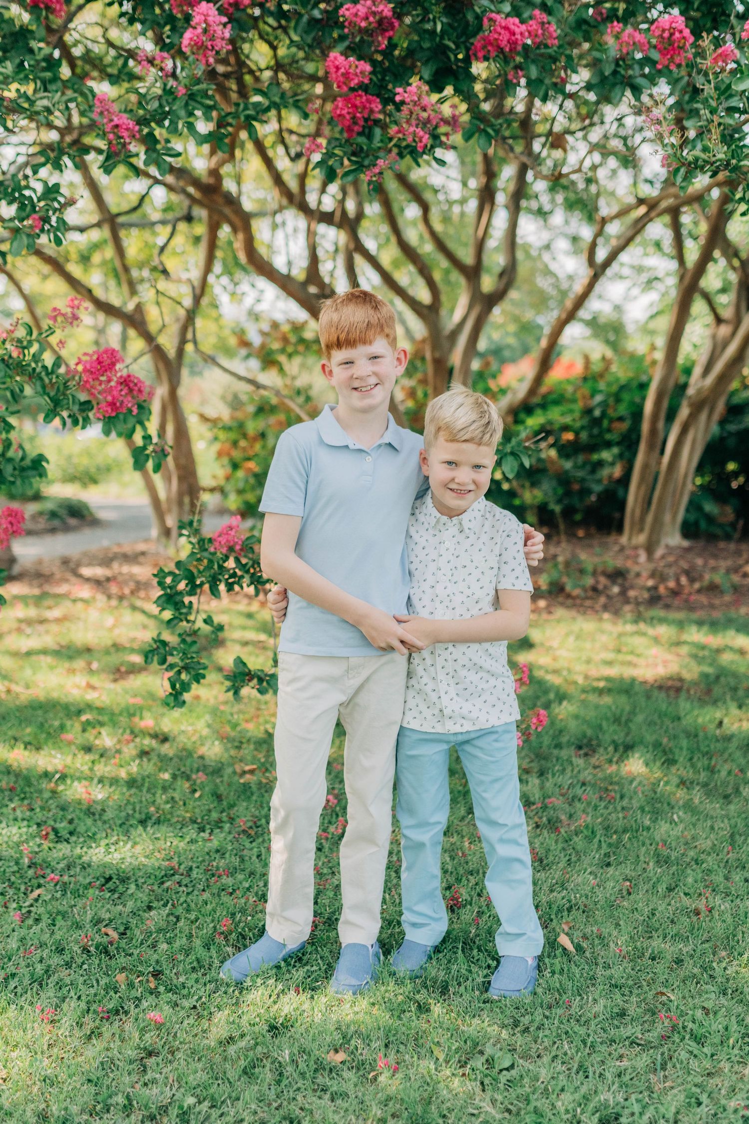 Siblings in coordinating outfits sharing sweet moments in a garden with pink flowers.