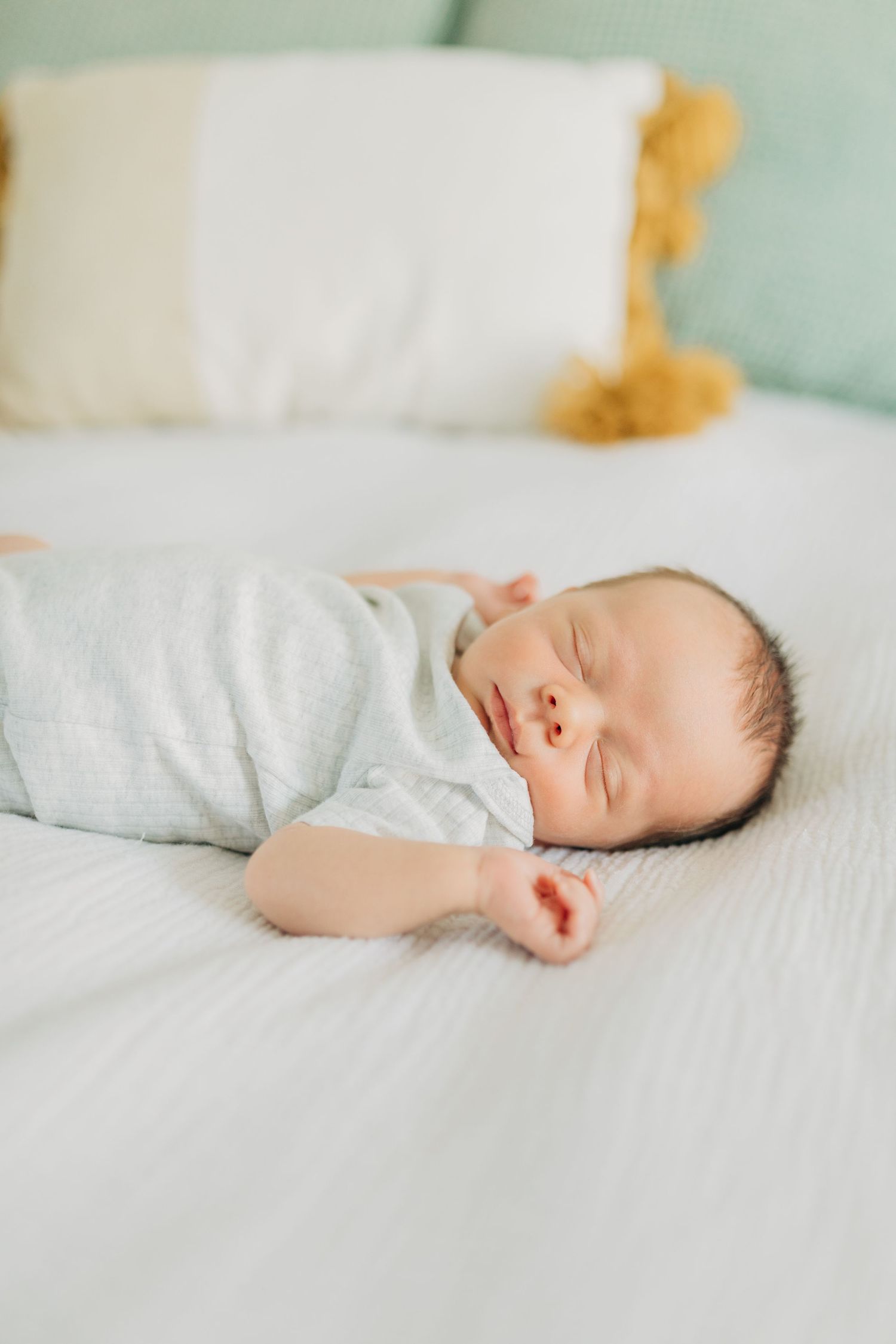 Sleeping newborn in grey outfit on white bedding with mint green accents.