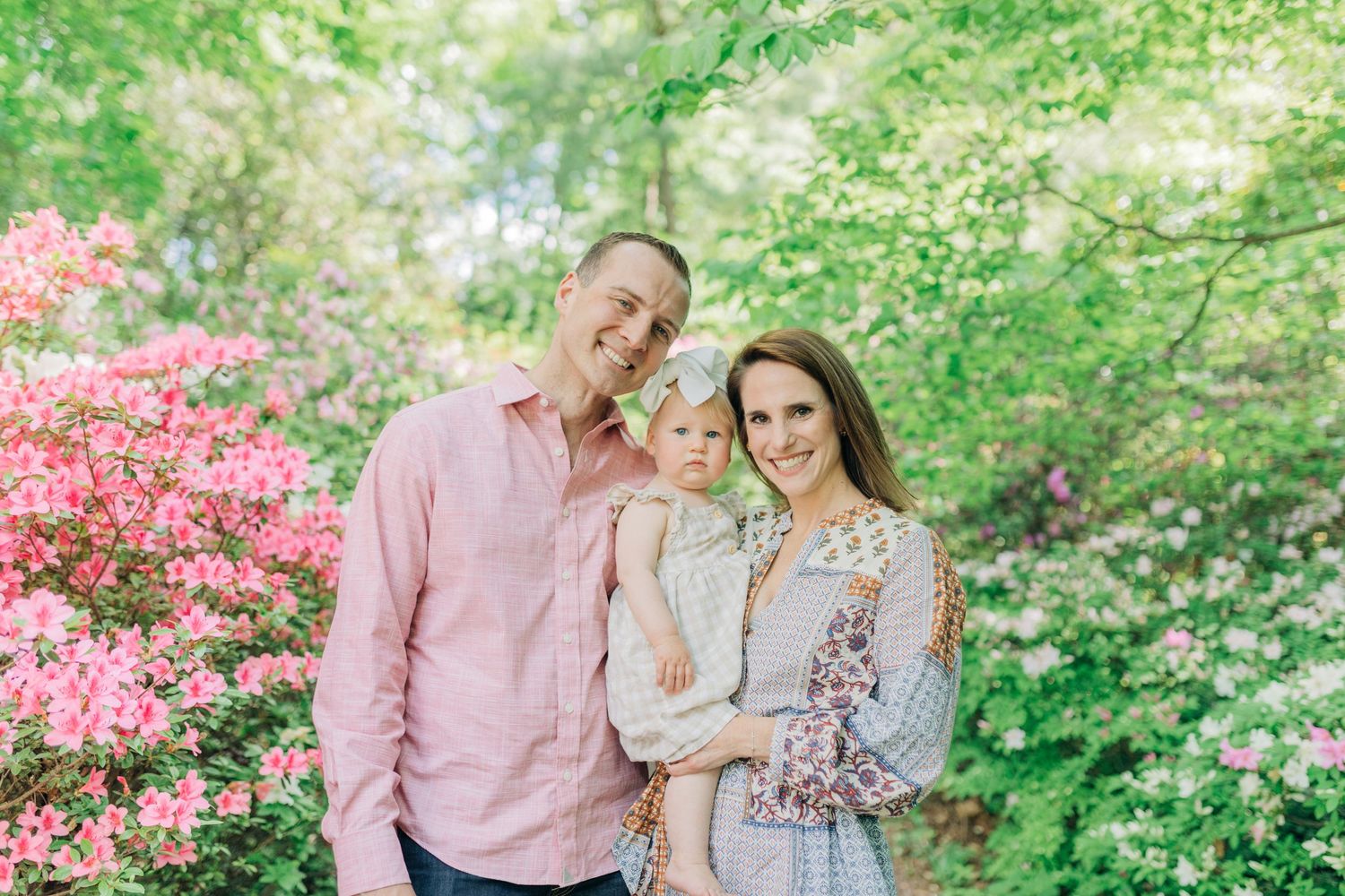Spring family photoshoot in garden with blooming azaleas and green trees.