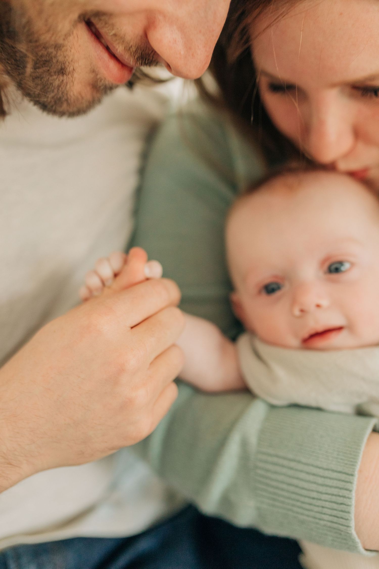 Close-up tender moments with baby in white onesie on bed.