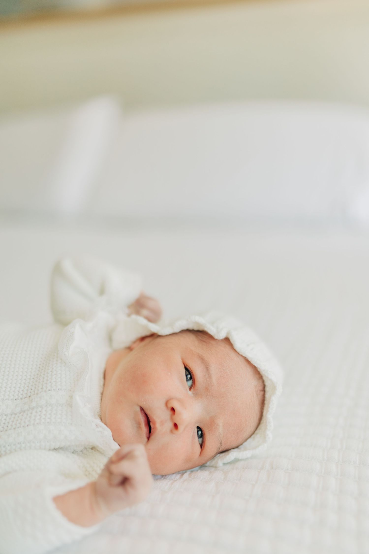 Close-up of infant in white bonnet lying on textured white fabric.