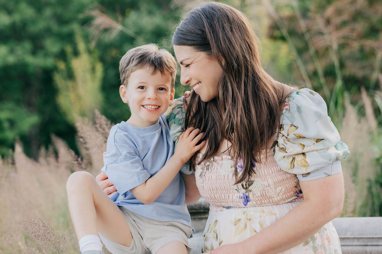 A young boy and his mother share a sweet moment outdoors, surrounded by lush greenery and wildflowers.