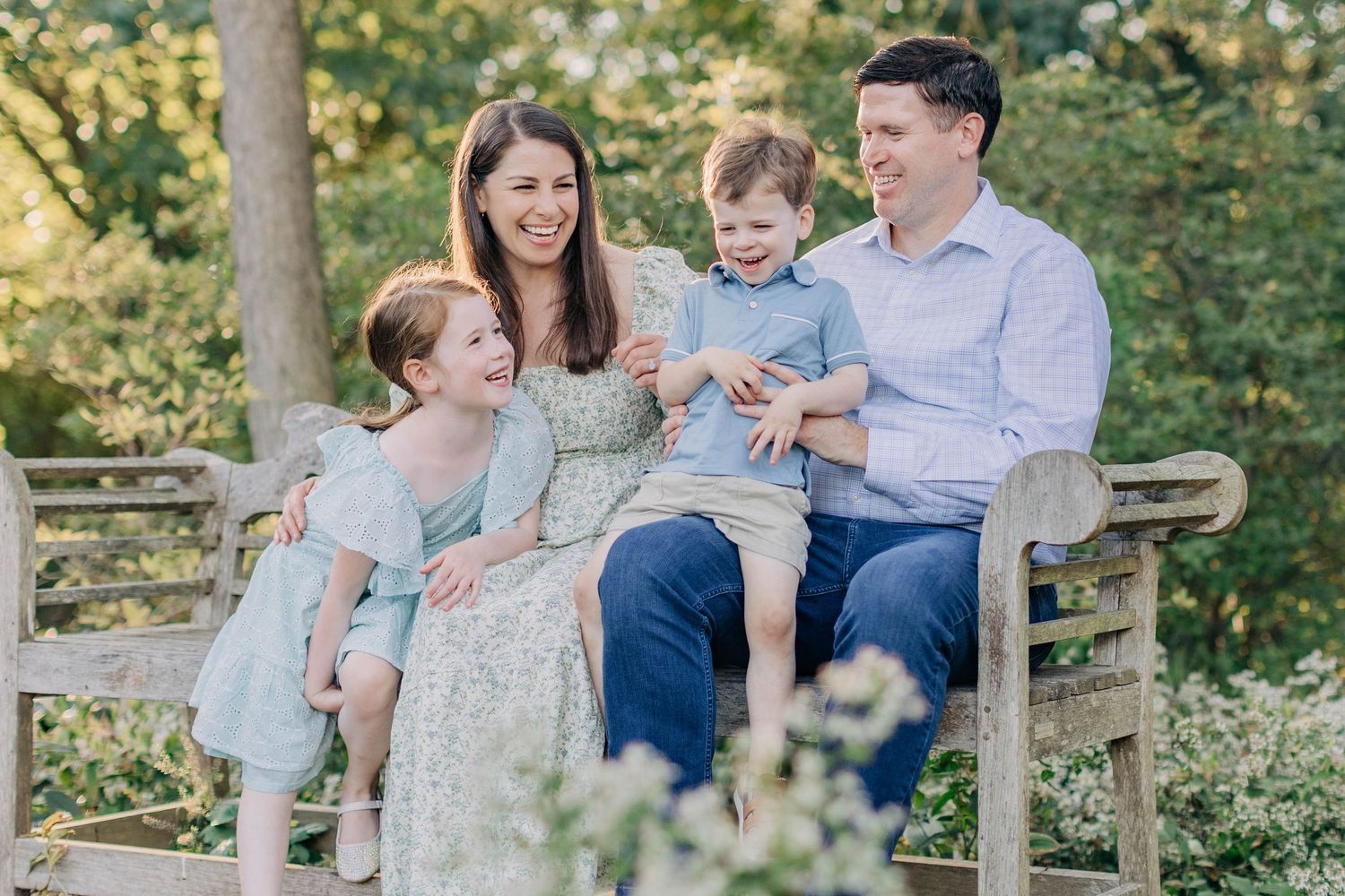 A family sits together on a wooden bench in a garden setting during golden hour.
