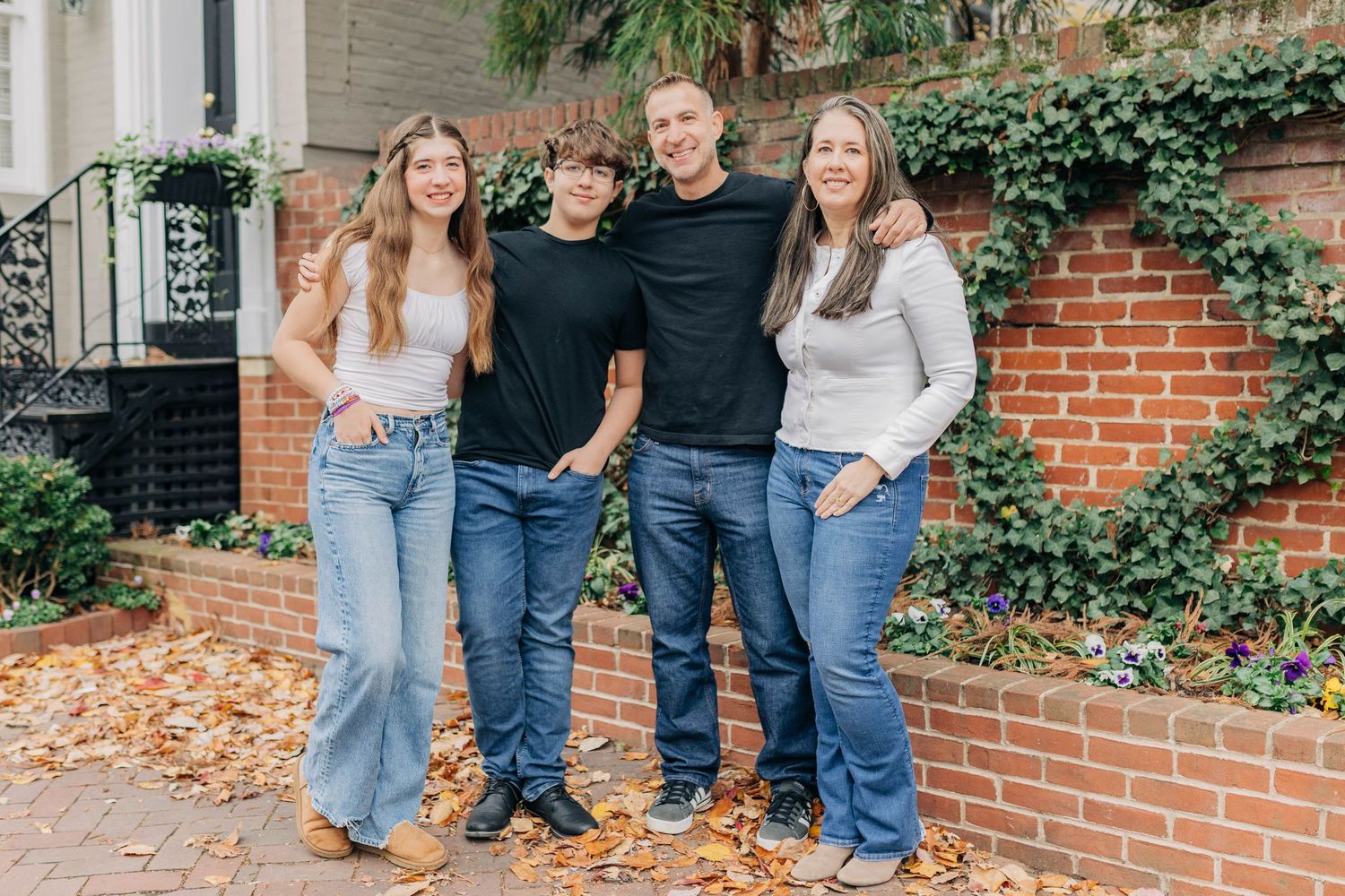 A casual group photo against a brick wall with ivy, wearing jeans and casual tops in an outdoor setting.