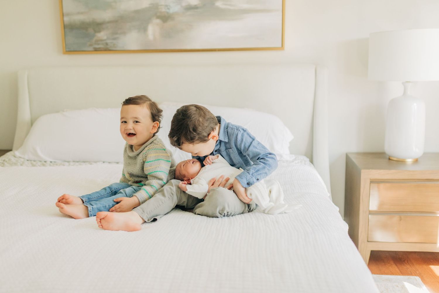 Three children enjoy quality time together on a bright white bed.