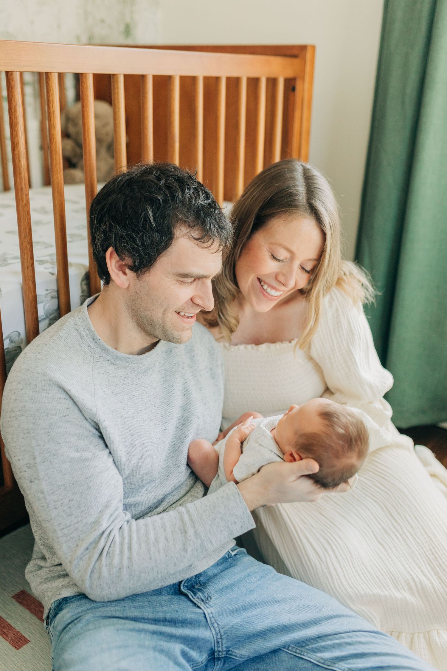 Candid family moment showing parents bonding with their newborn on white bedding.
