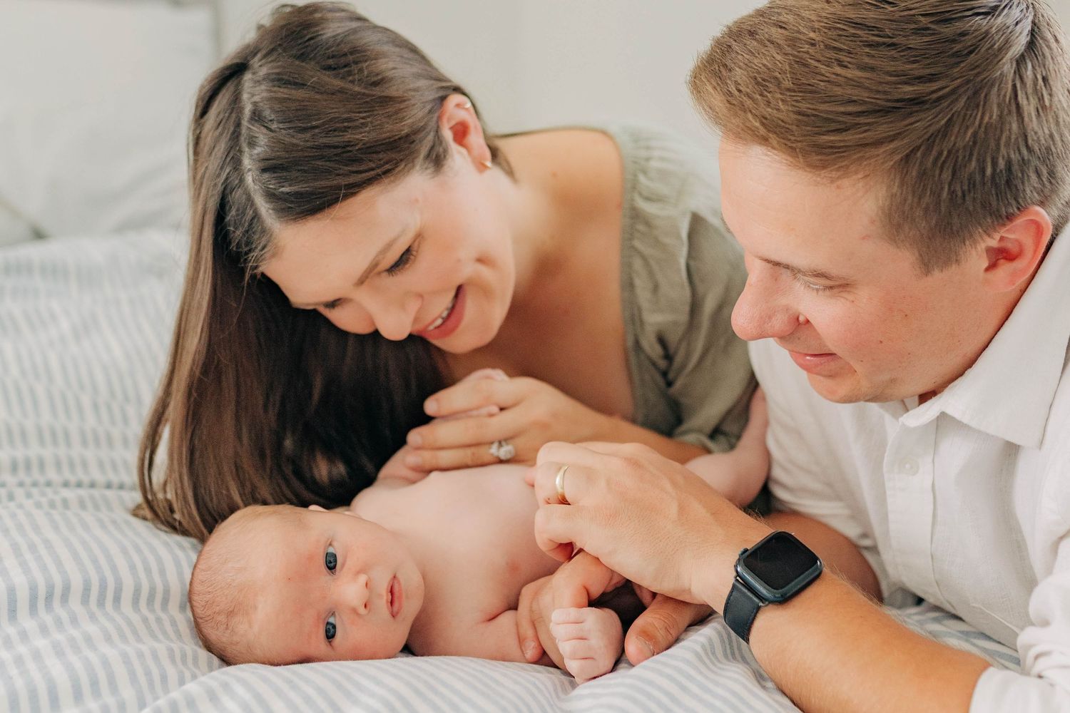 An intimate family portrait session with soft lighting on white bedding.