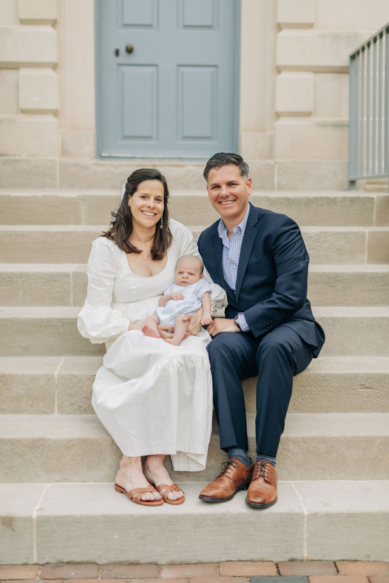 Family of three poses together on stone steps in formal attire.