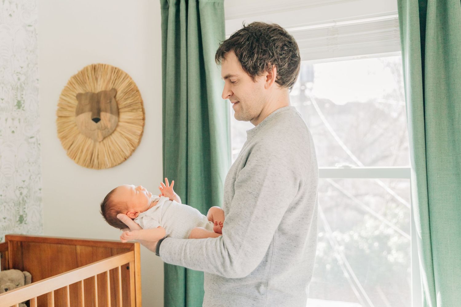 A tender moment between parent and newborn in a bright nursery with wooden crib.