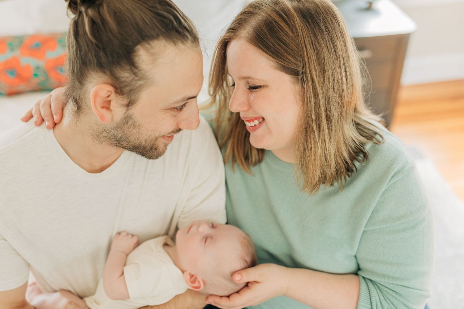 Parents in casual clothing bonding with their infant on a bright bed.