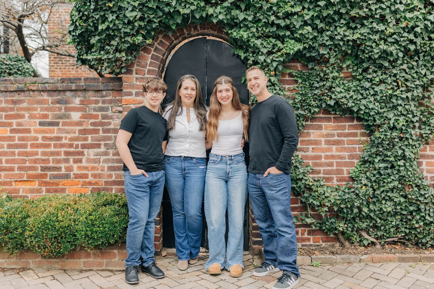 Family portrait session against a rustic brick wall covered in ivy.