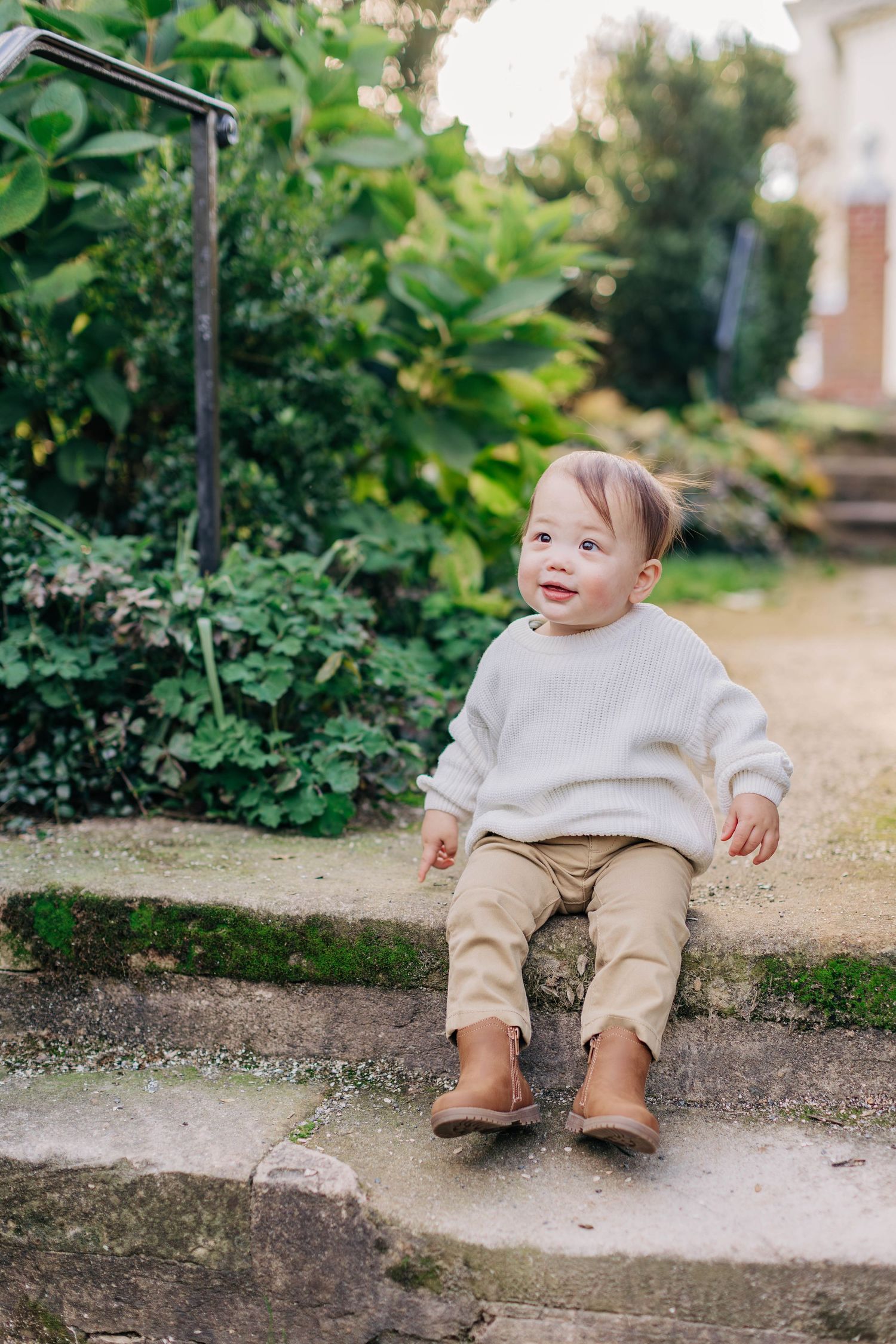 Toddler in beige outfit sitting on concrete steps during outdoor photoshoot.