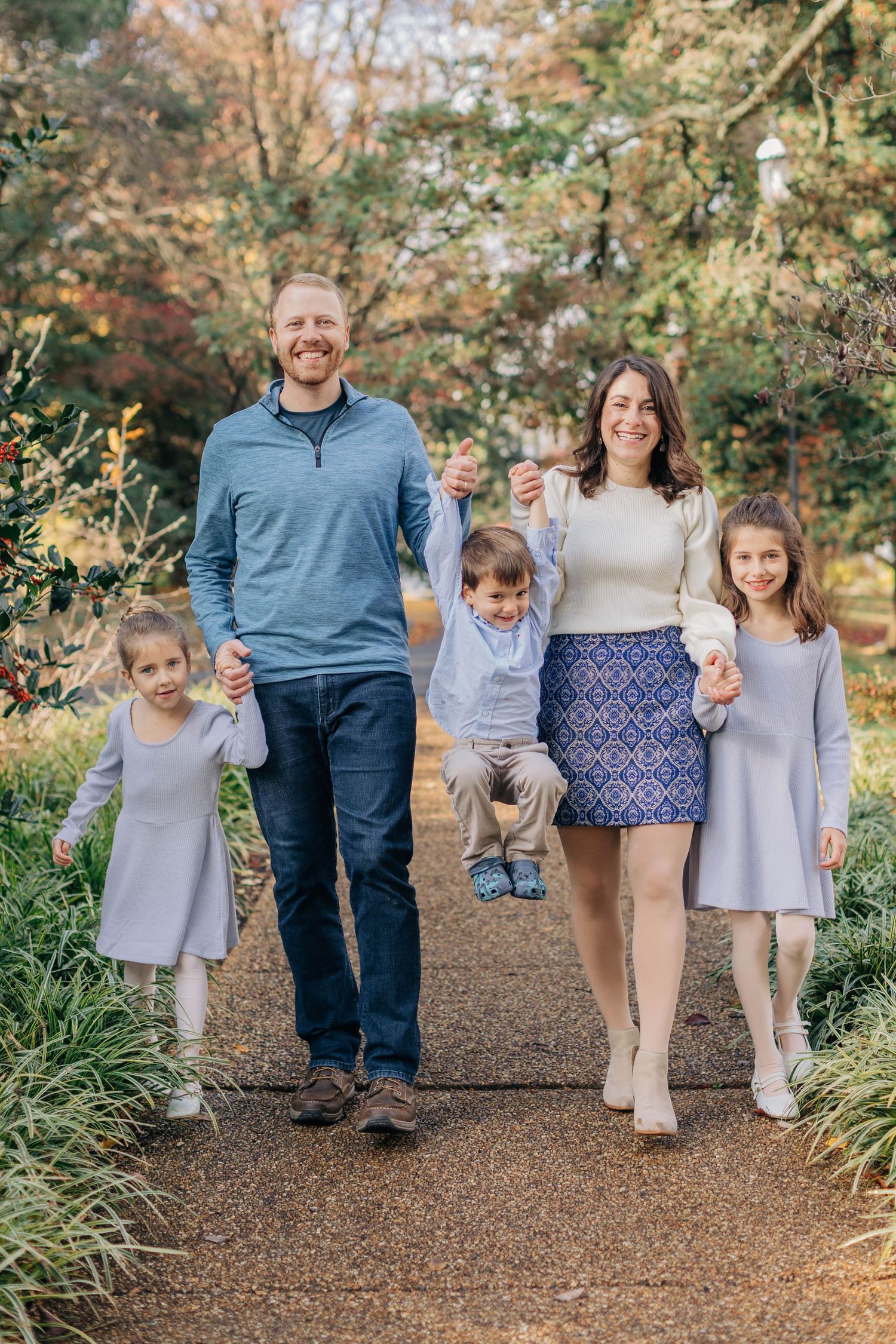 A cheerful family of five poses together on a garden path surrounded by fall foliage.