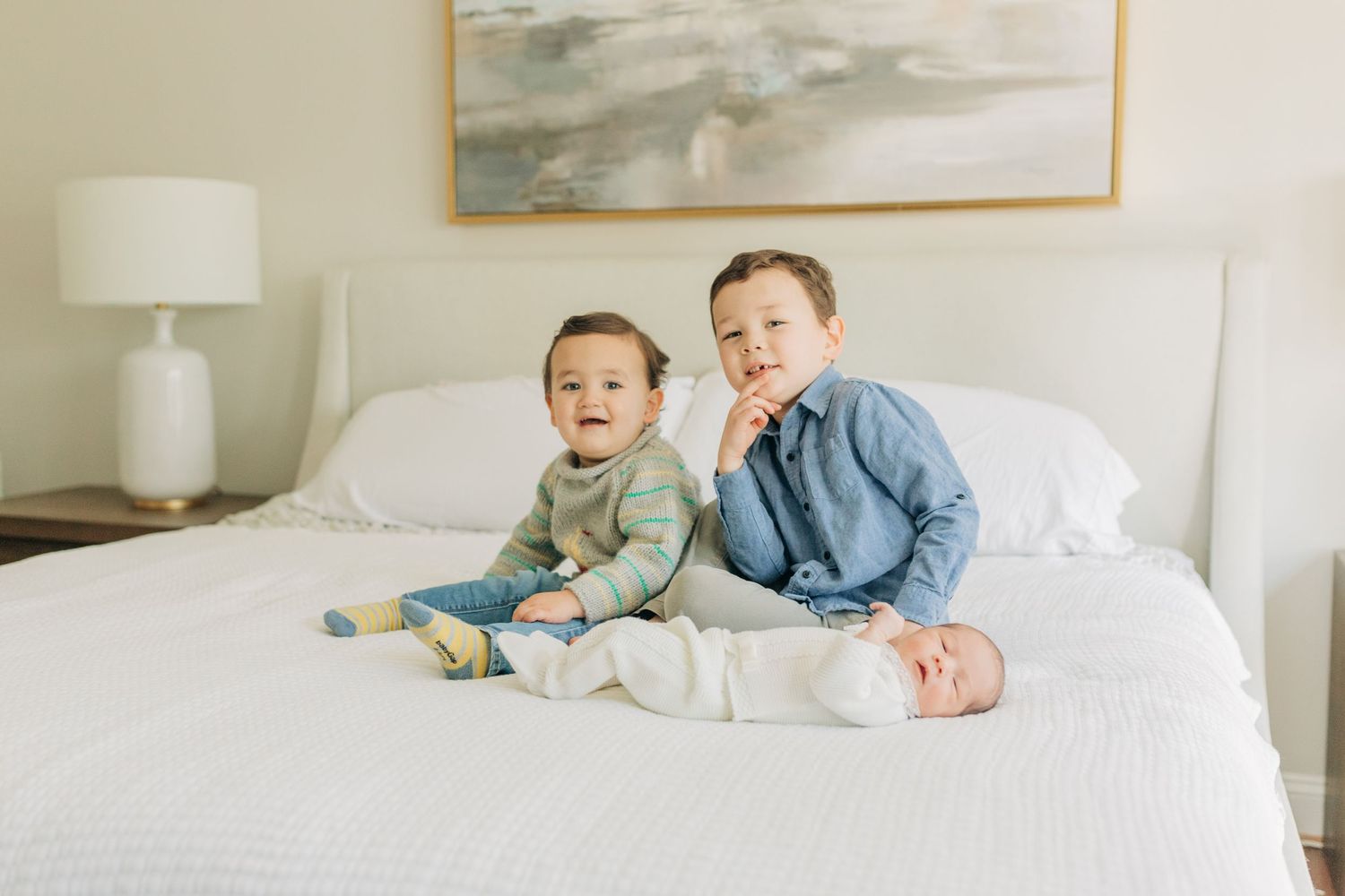 Siblings share tender moments together on white bedding in a bright room.