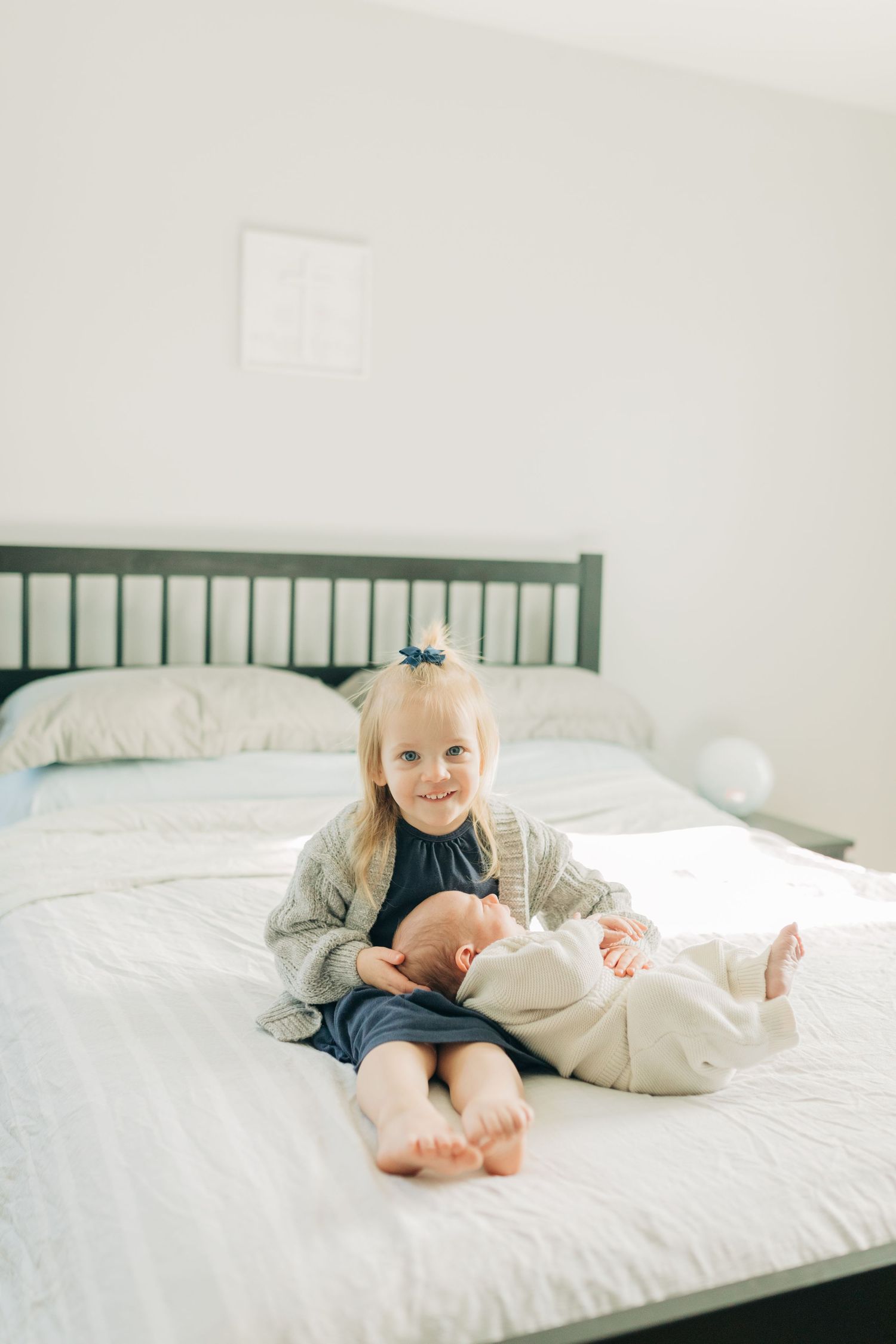 Two siblings share a sweet moment together on a bed with a green headboard.