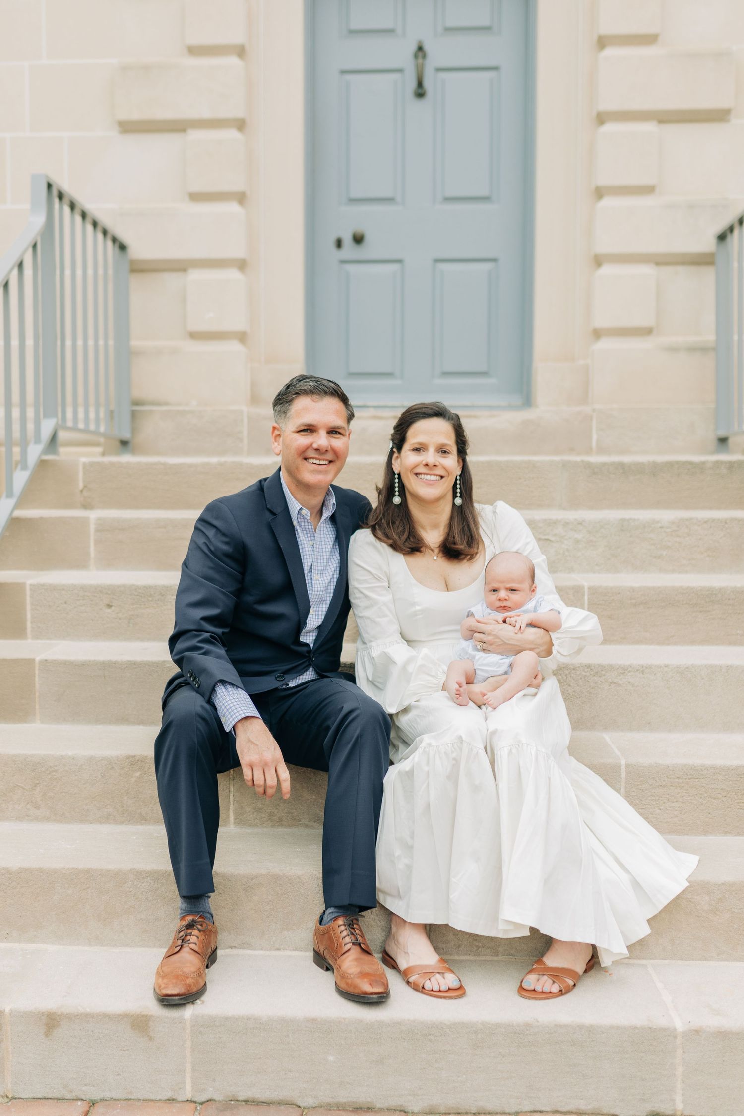 Family portrait on stone steps with light blue door and classic architecture.