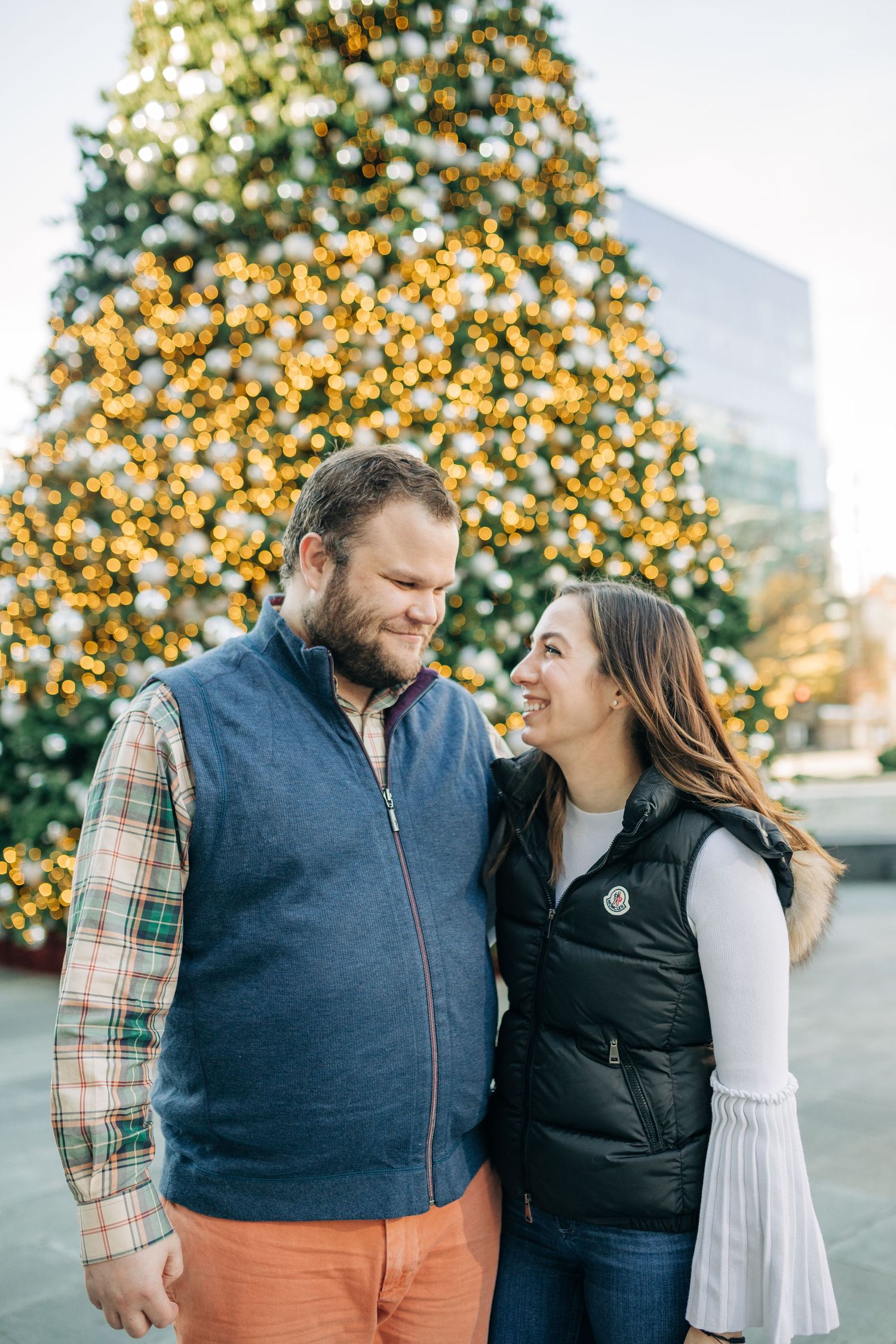A couple shares a joyful moment together in front of holiday lights and greenery.