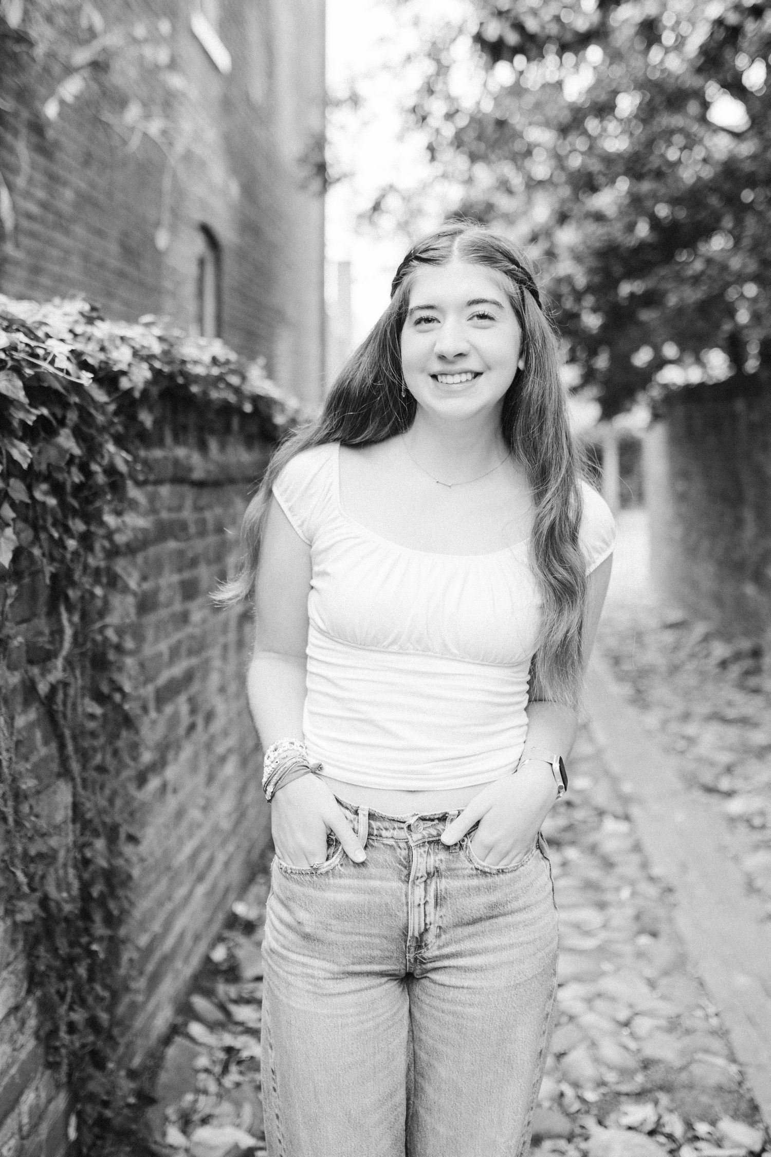 Black and white portrait of a person in casual attire smiling against a brick wall background.