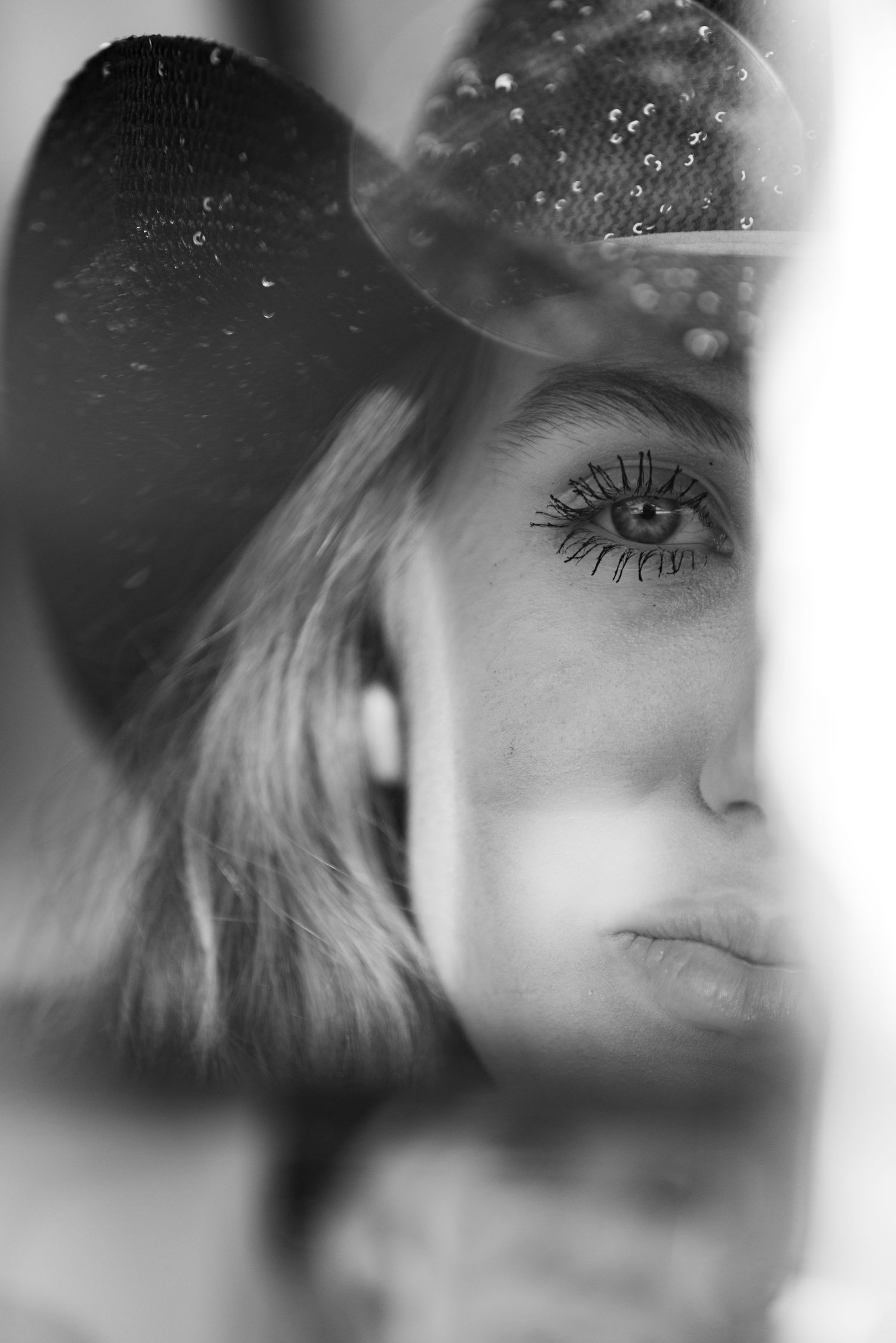 Black and white portrait of a woman in a cowboy hat, captured through a mirror with striking eye detail.