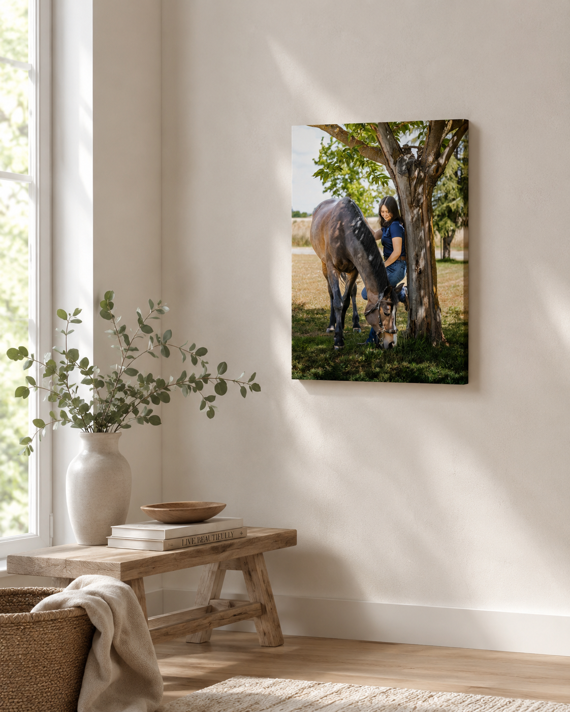 Canvas wall art of a person with a dark horse under a tree in a sunny field, displayed in a bright, minimalist room.