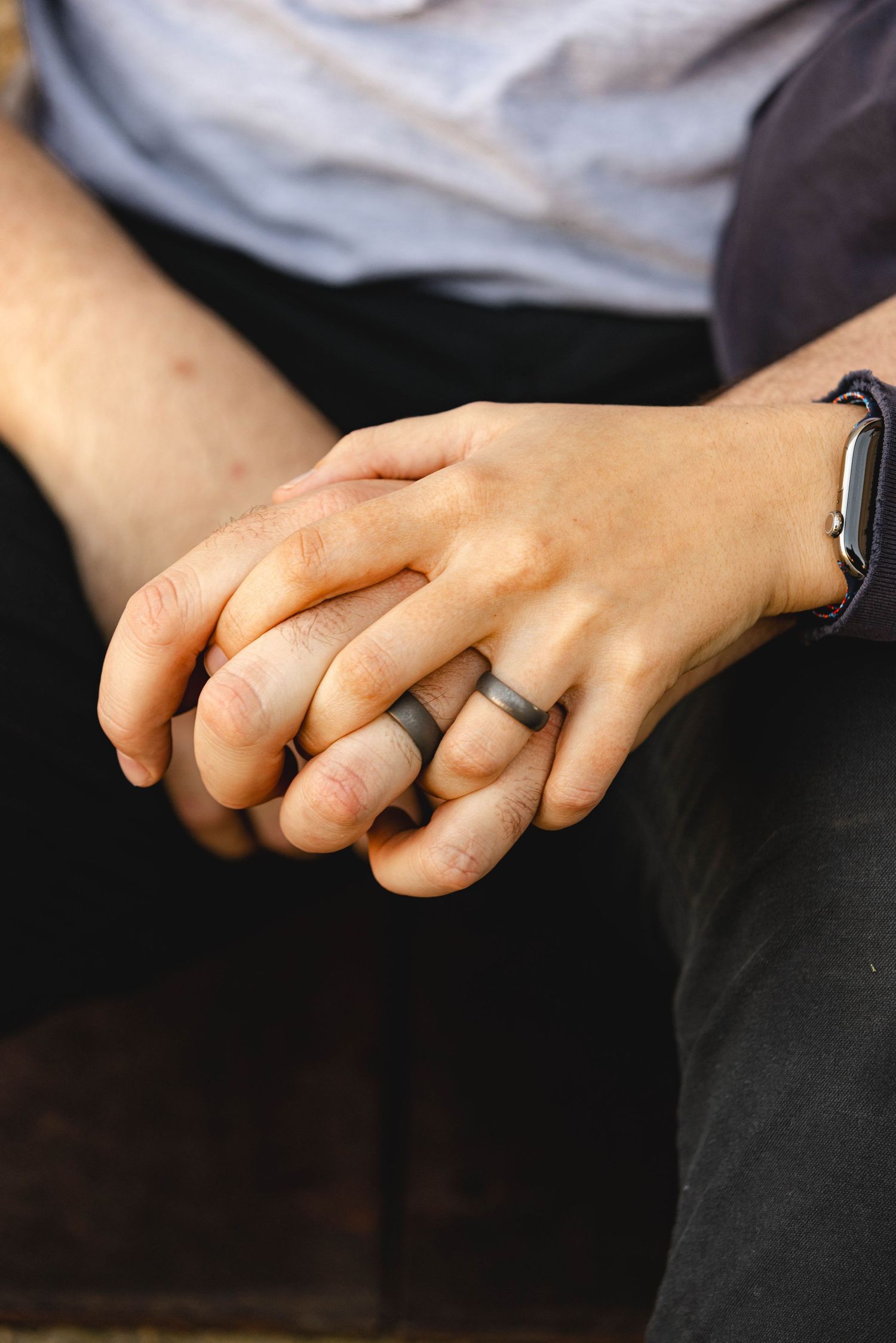Couple holding hands with matching dark silicone wedding rings, one wearing a smartwatch.