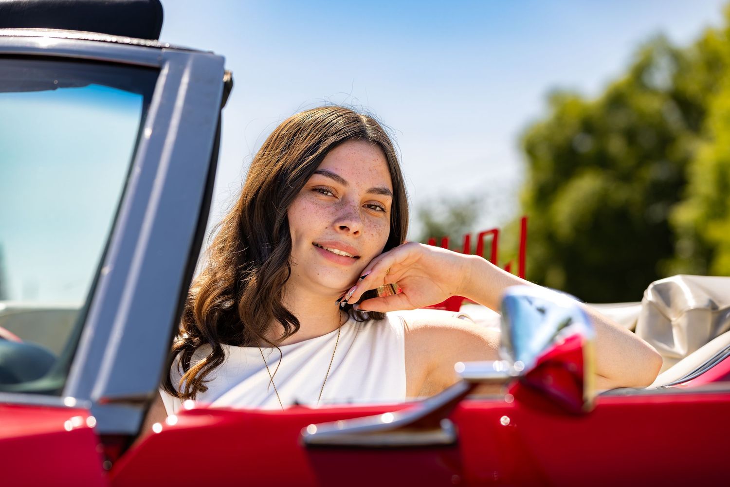 Young woman with brown hair relaxing in red convertible car on sunny day with blue sky.