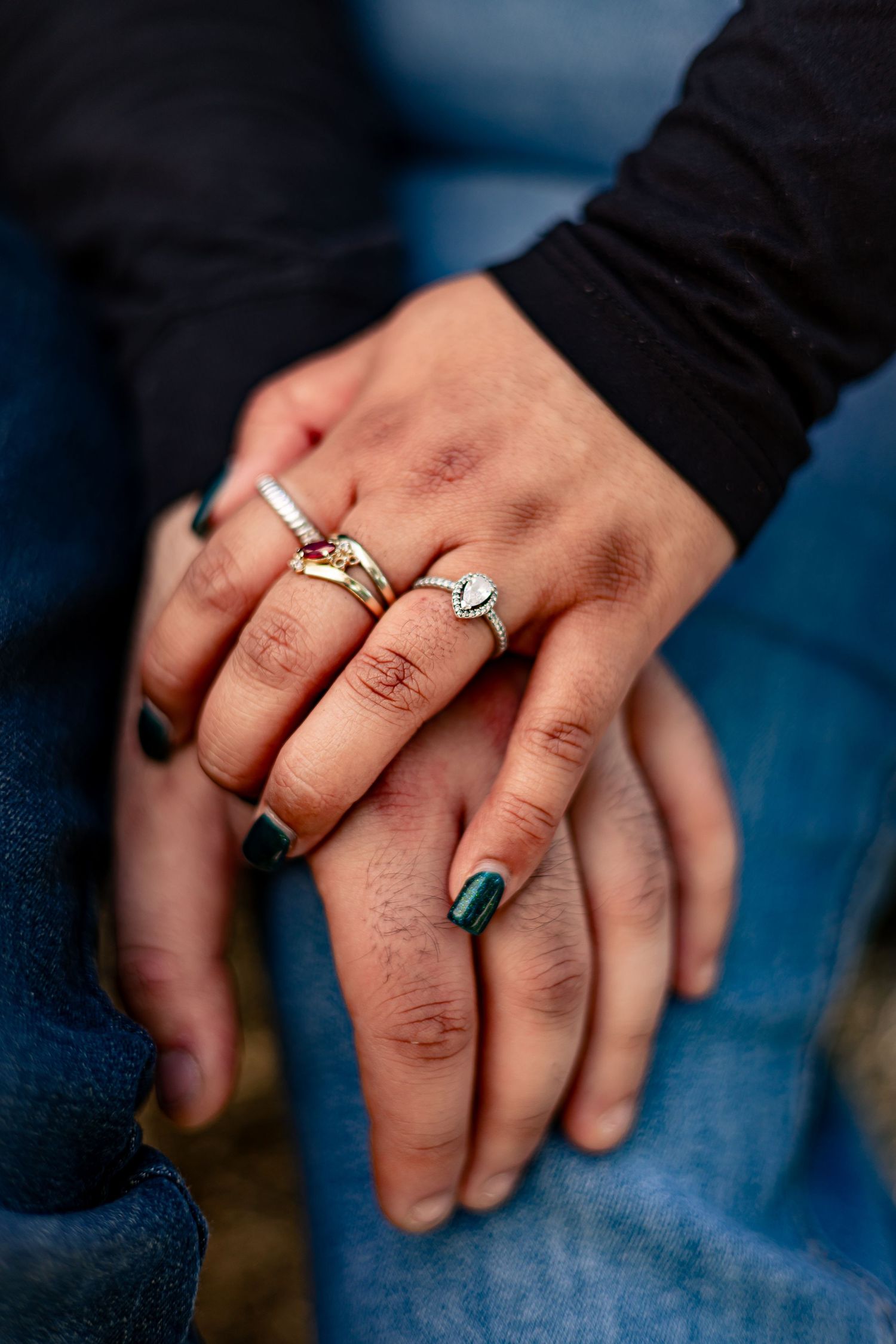 Close-up of couple holding hands showing elegant rings with dark nail polish outdoors.