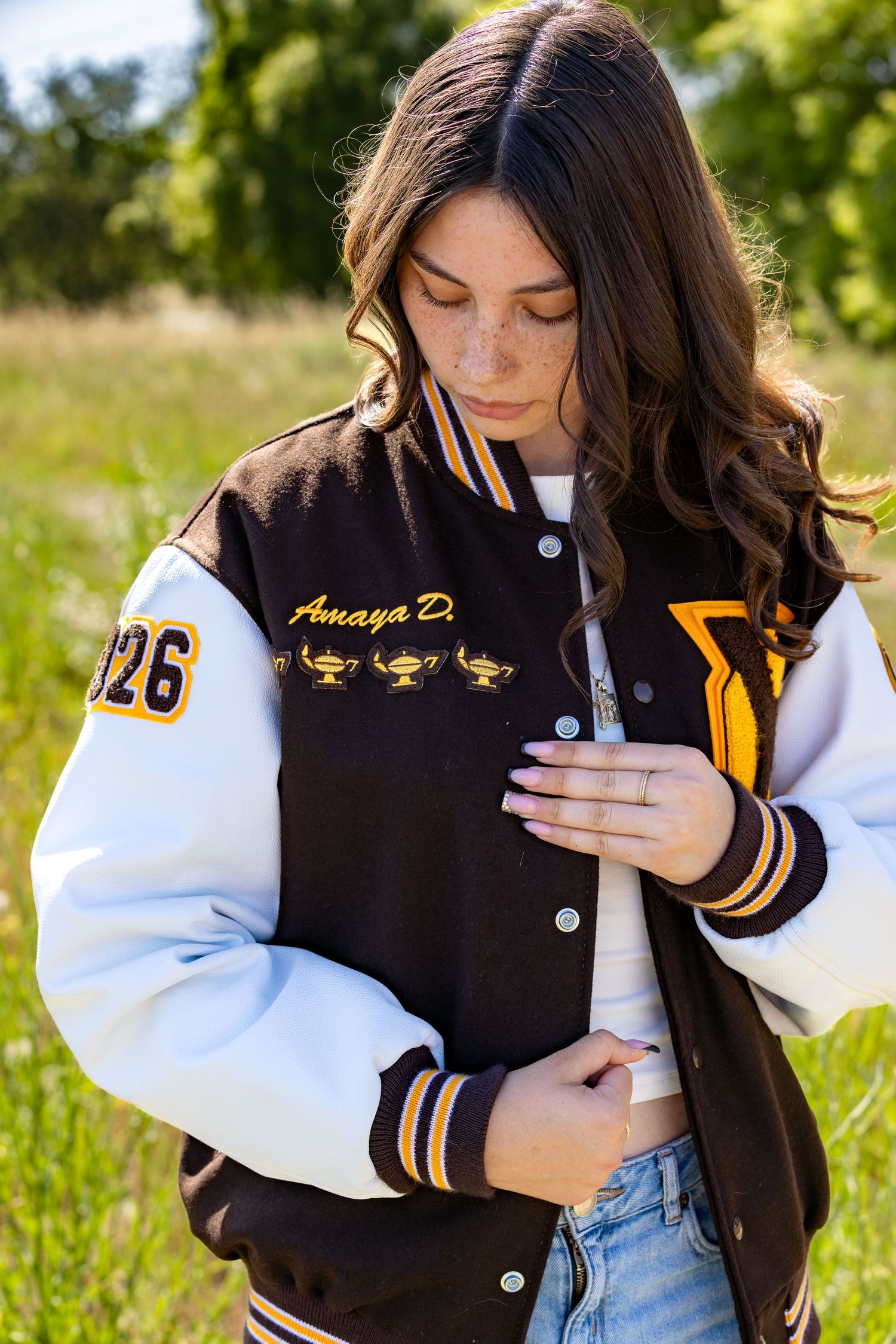 Young woman wearing a custom brown and white varsity letterman jacket with gold embroidery outdoors.