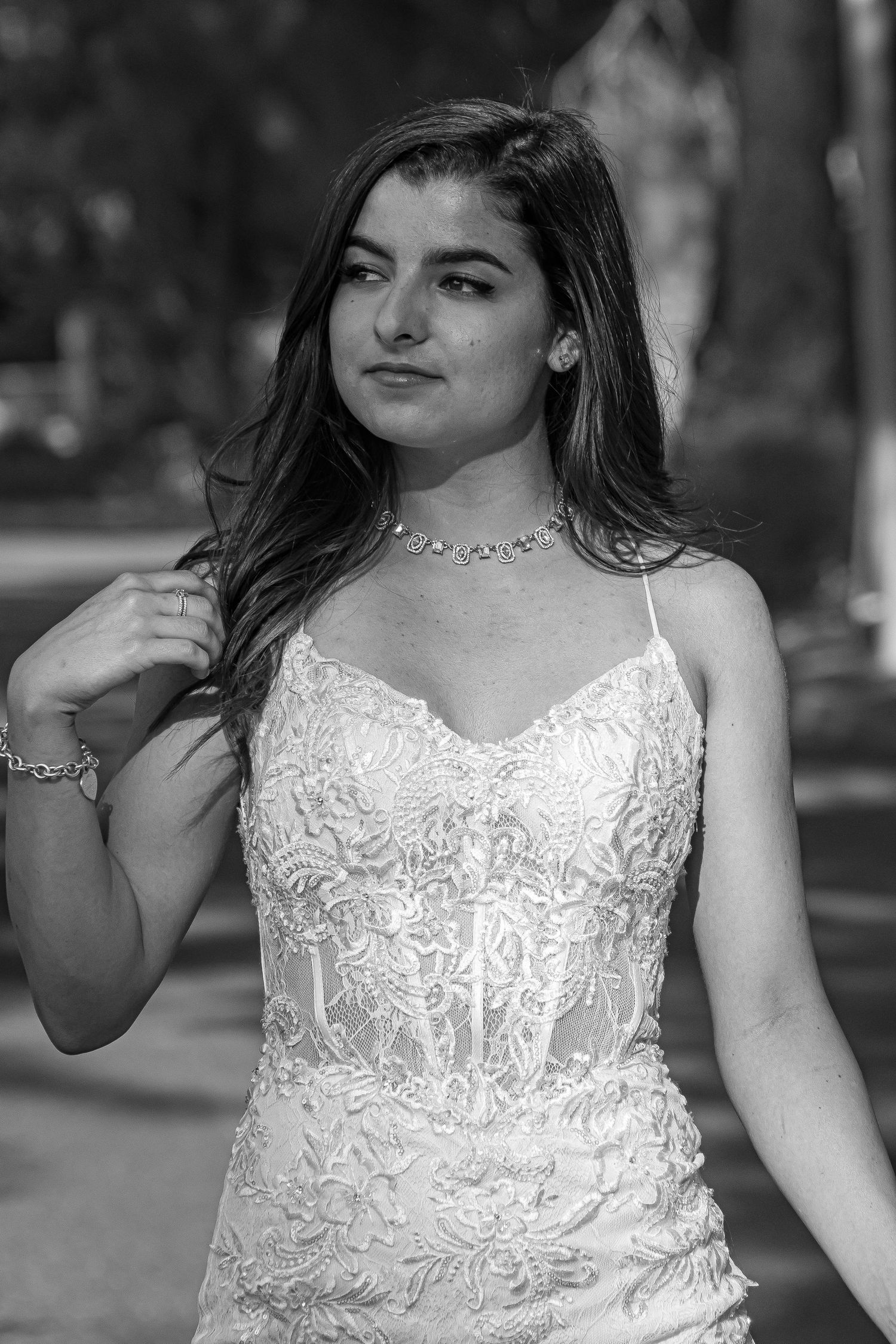 Young woman in lace spaghetti strap dress and choker necklace poses outdoors in black and white portrait photo.