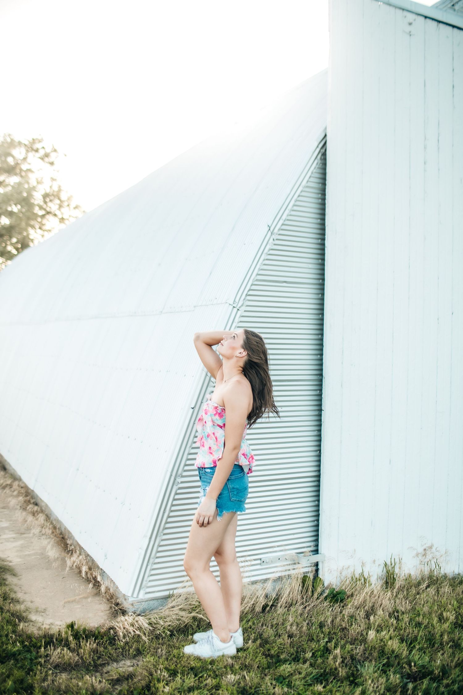 Summer portrait session against white industrial building wearing colorful top.