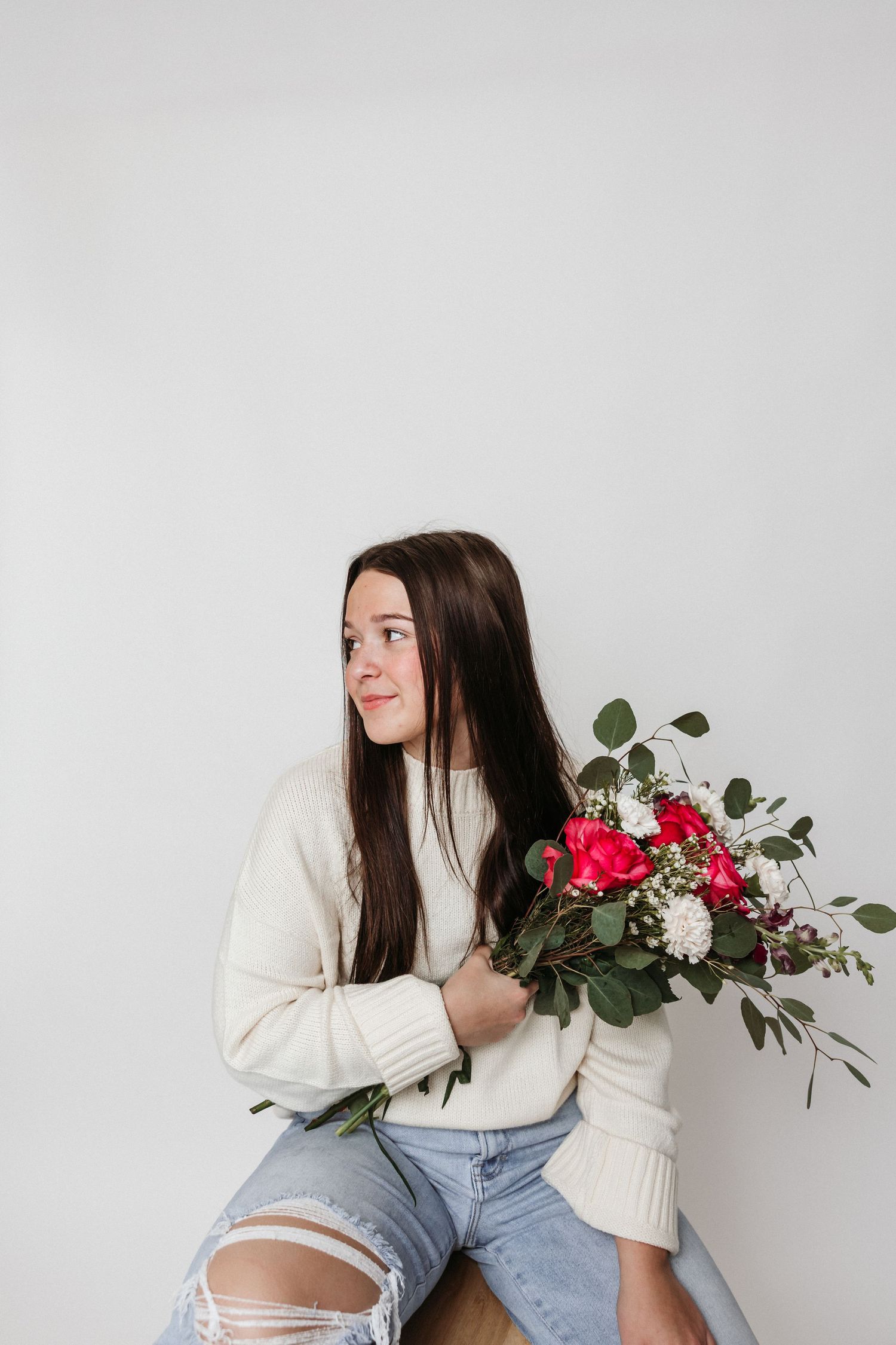 Candid moment with floral bouquet sitting on wooden stool against white background.