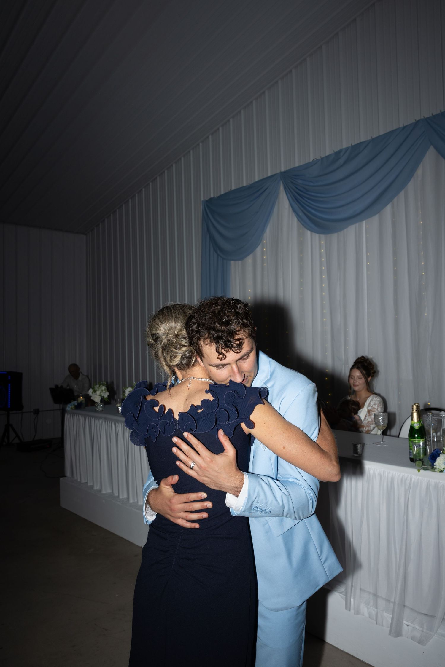 Couple sharing a romantic dance embrace at a wedding reception with blue draped decor in background.