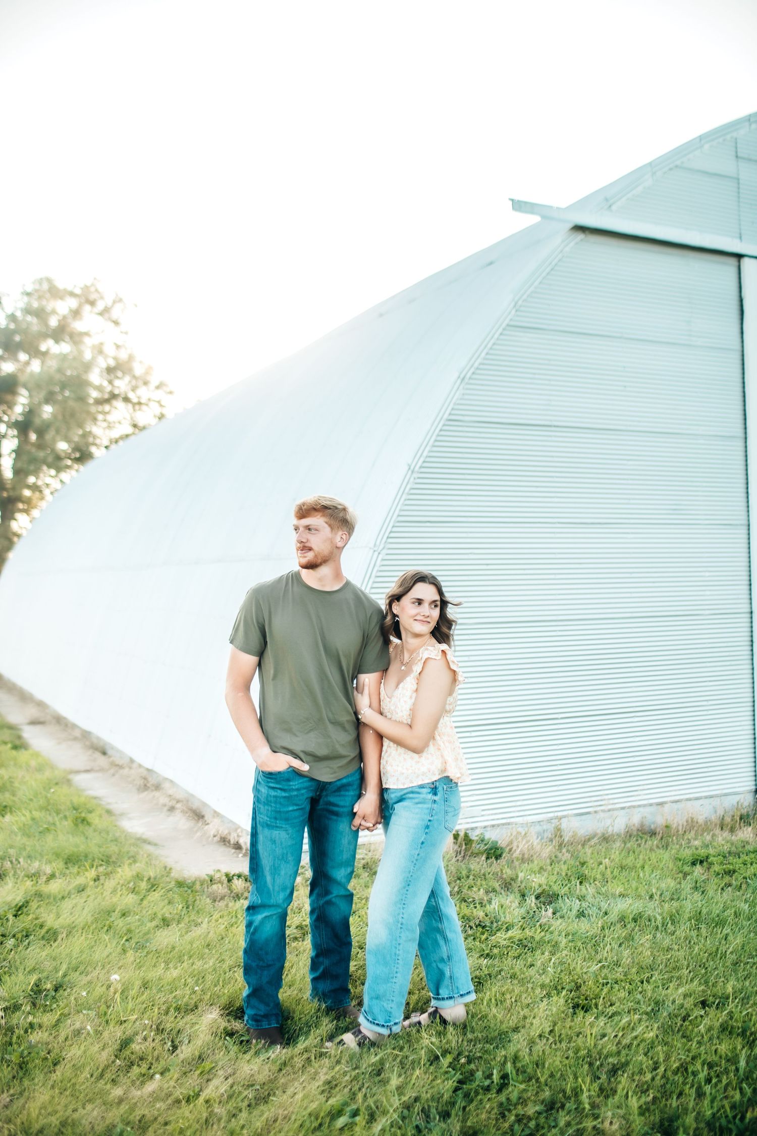 A couple stands together against an architectural structure on a grassy plain.