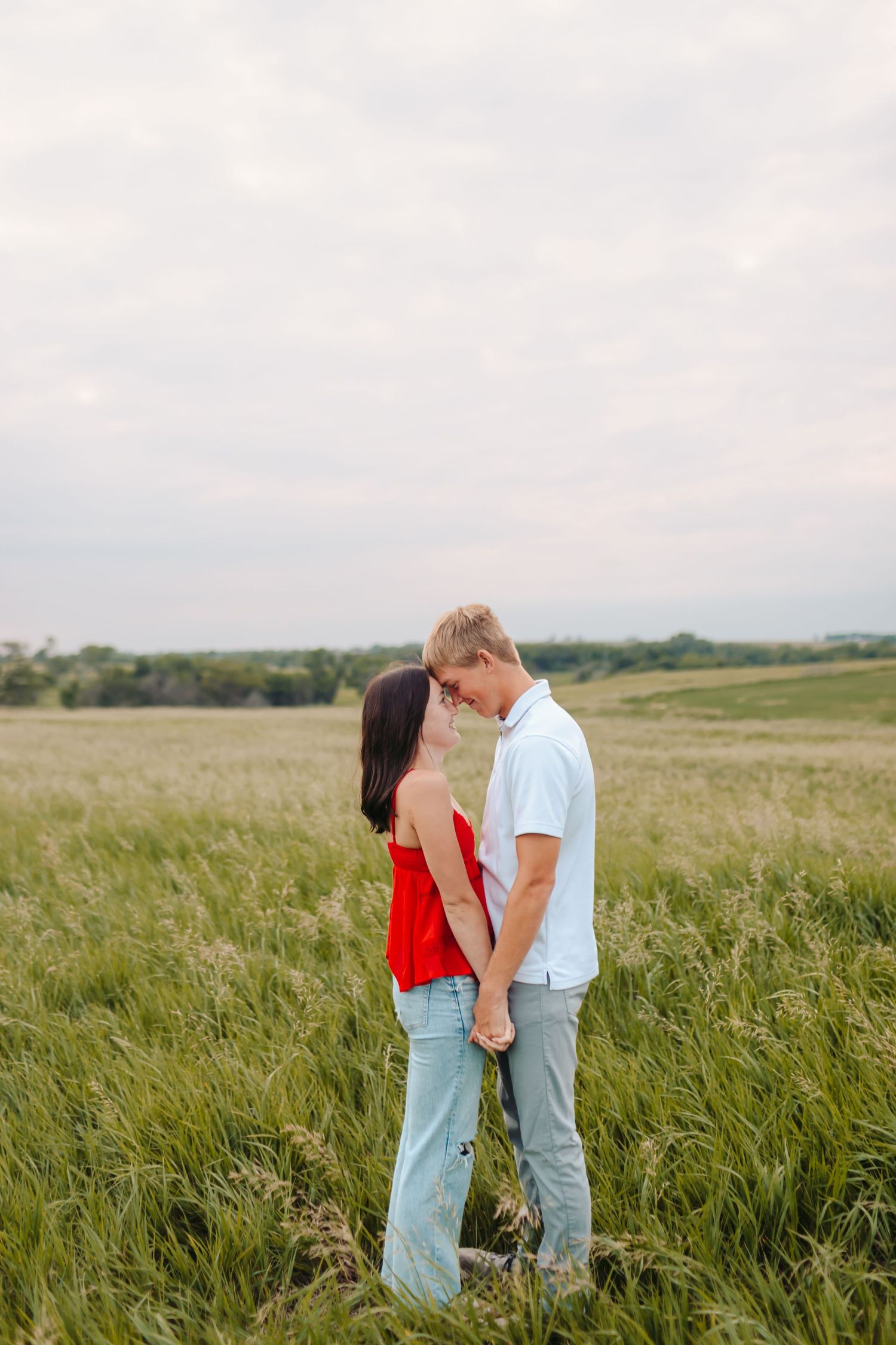 Intimate moment between couple standing in a grassy field during golden hour.
