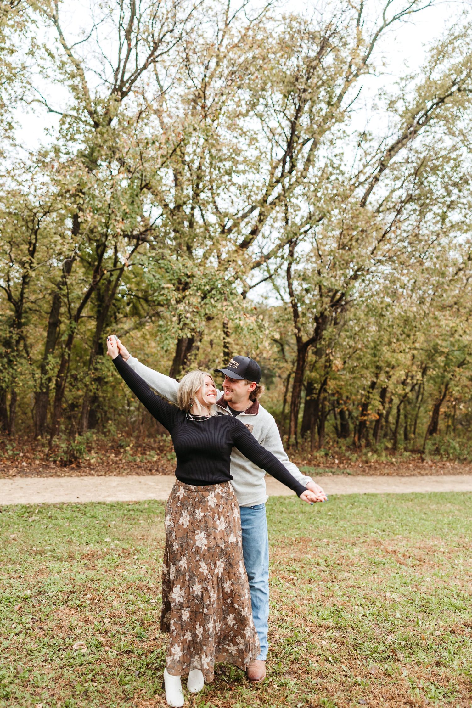 A playful couple dances together on fallen leaves in an autumn park.