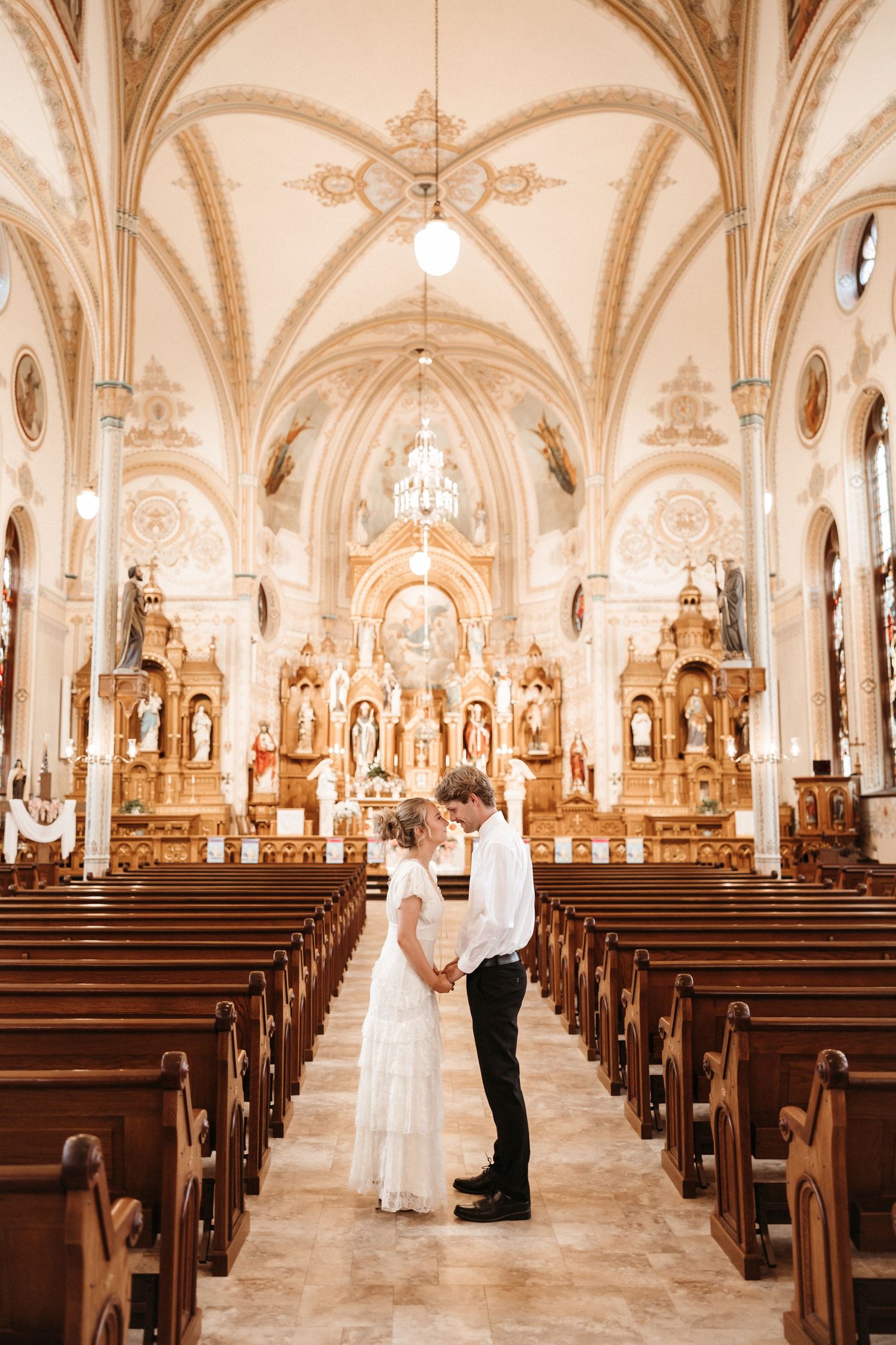 Couple holding hands at the altar of an ornate Catholic church with vaulted ceilings and wooden pews.