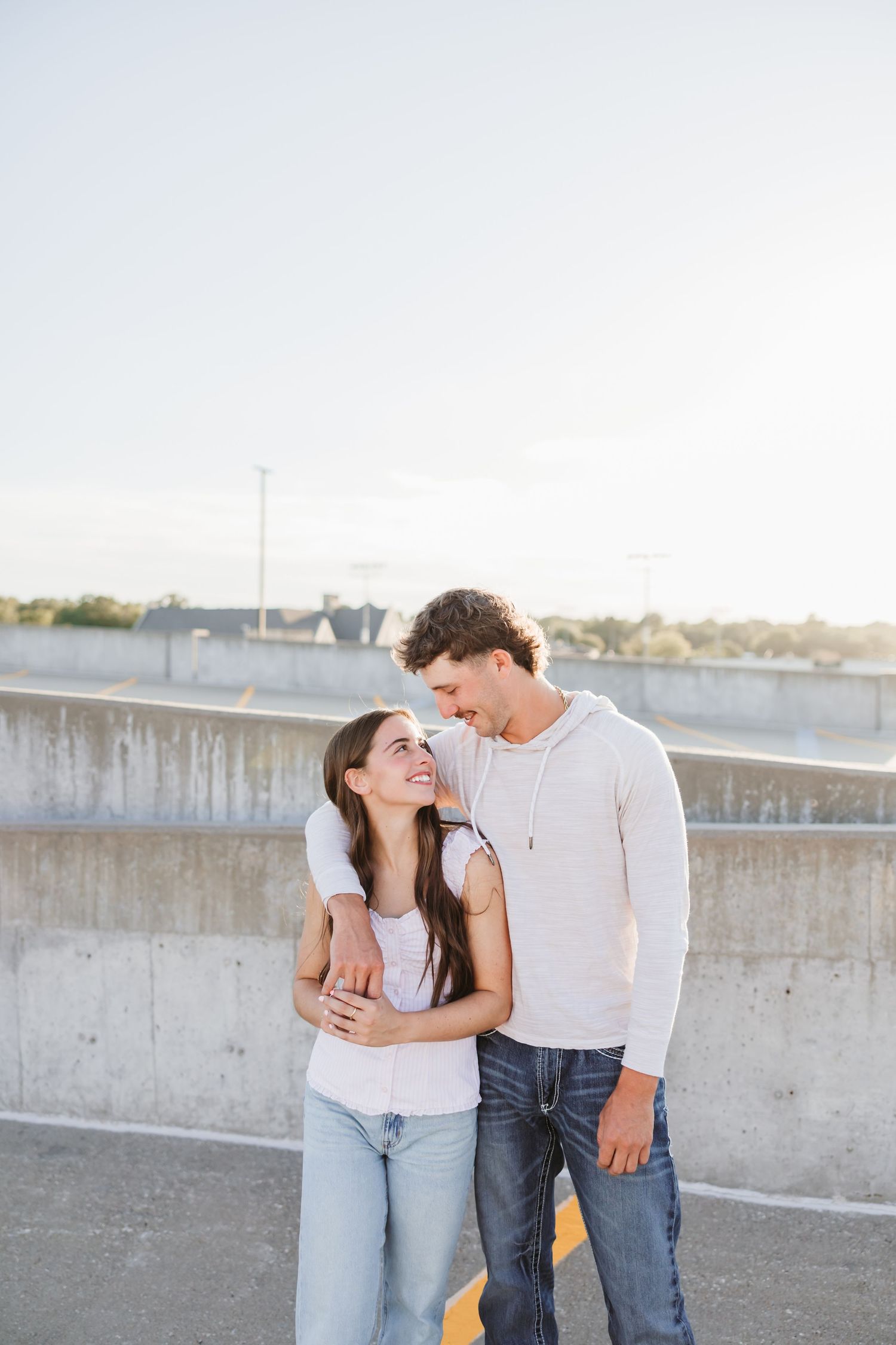 Couple in casual wear embracing on concrete parking garage at sunset.