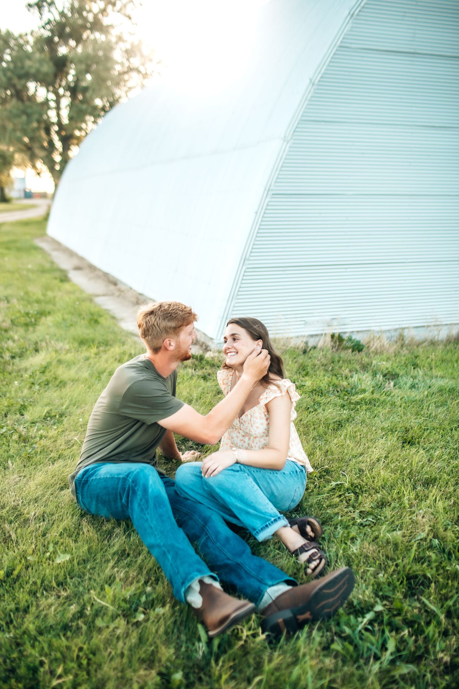 A tender moment shared between a couple sitting on grass beside a structure.